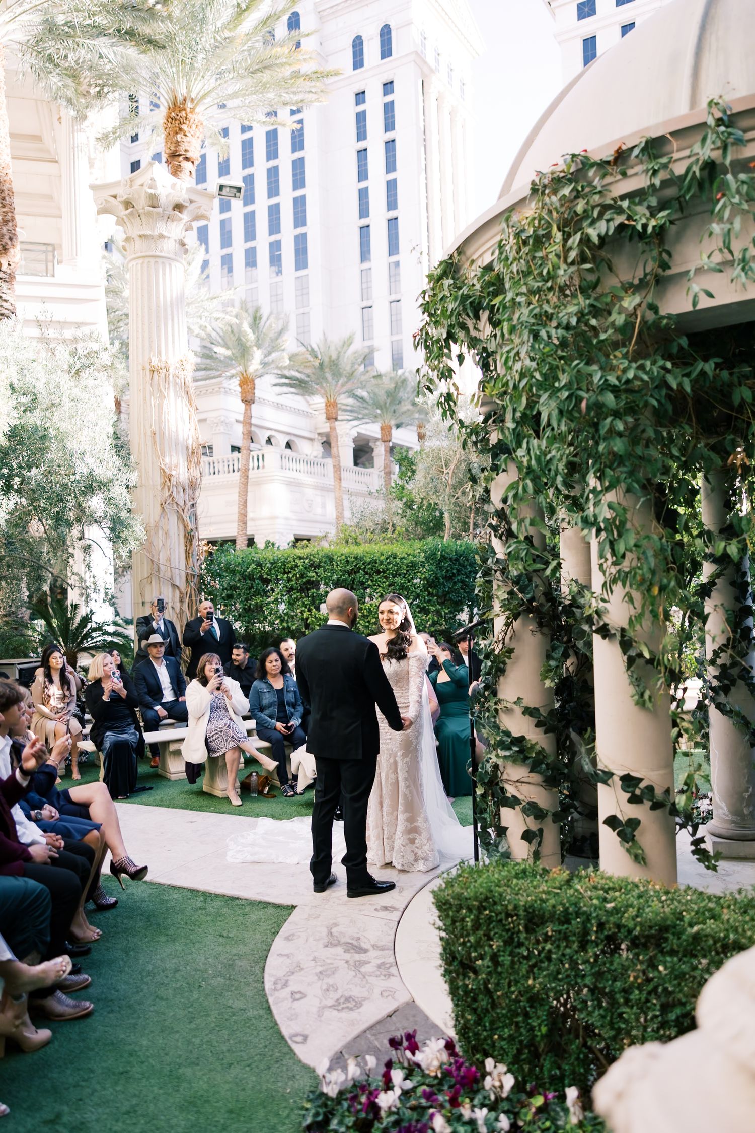 Couple exchanging vows at outdoor Las Vegas wedding ceremony surrounded by lush greenery and guests.