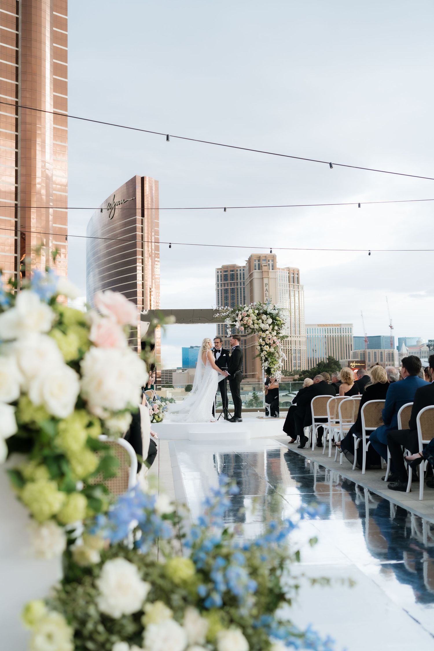 Elegant rooftop wedding ceremony with floral arrangements, mirrored aisle, and city skyline backdrop.