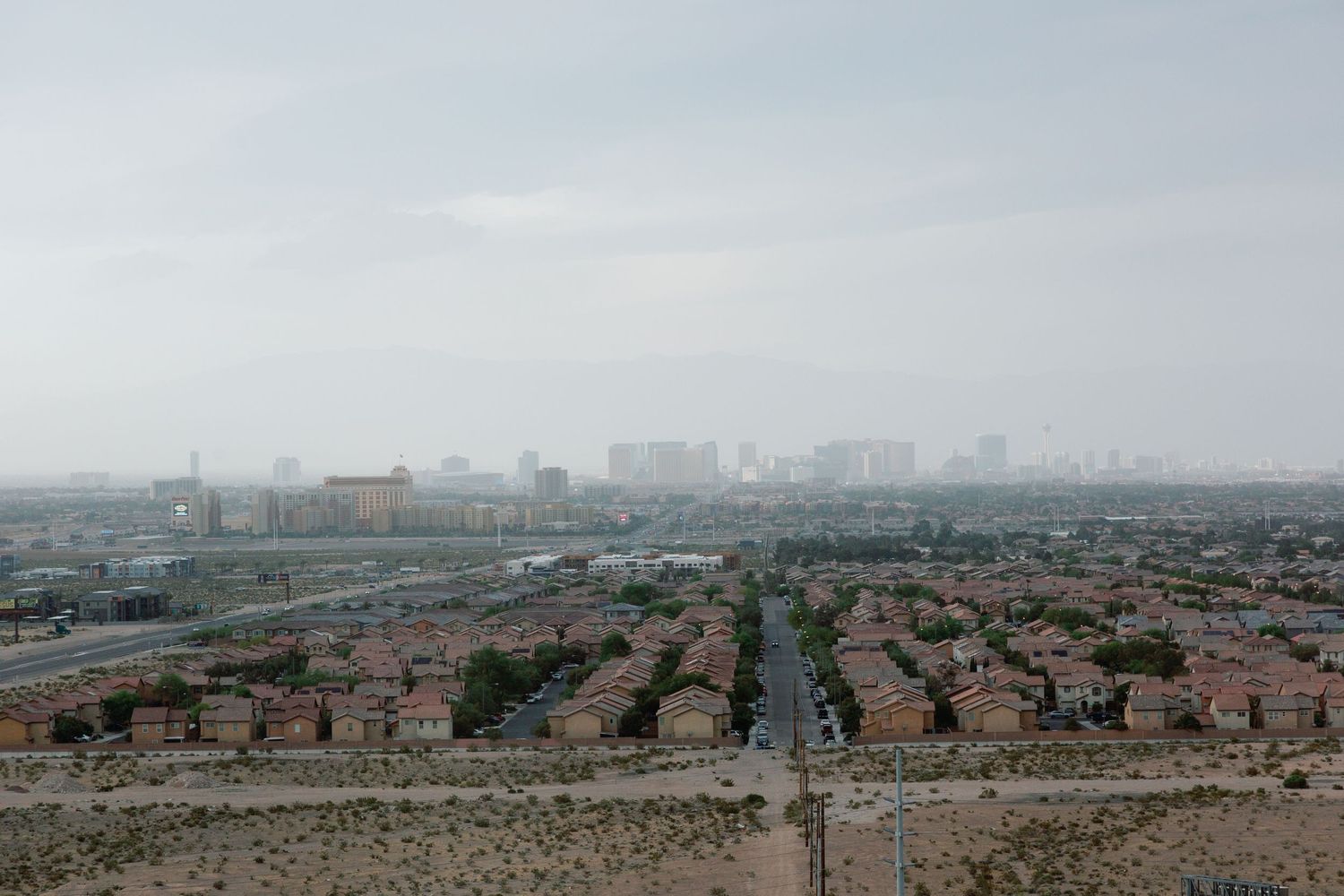 Aerial view of a sprawling suburban neighborhood with dense housing developments leading to a hazy city skyline.
