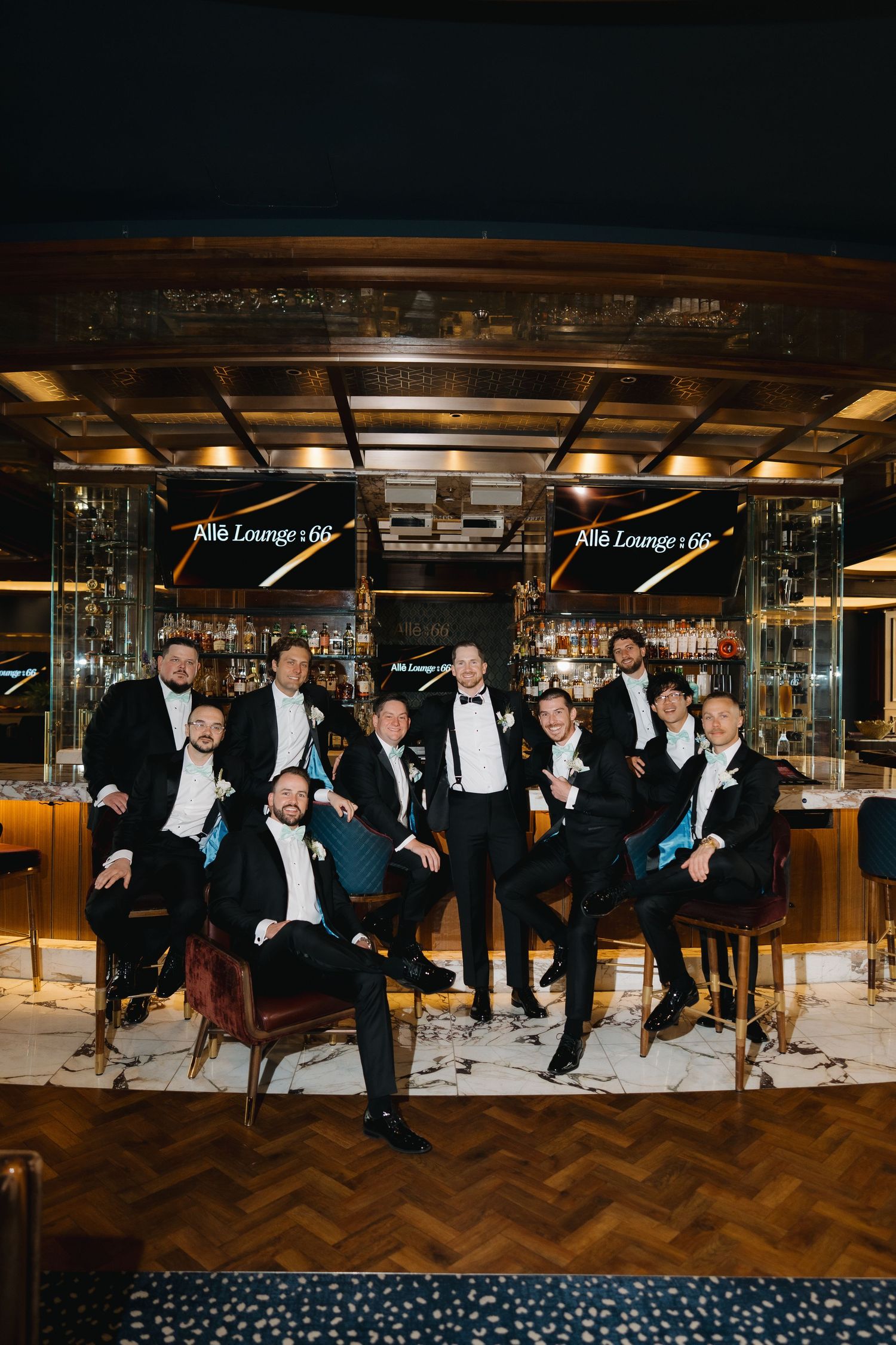 Groom and groomsmen pose together in black tuxedos at a stylish upscale bar lounge venue.