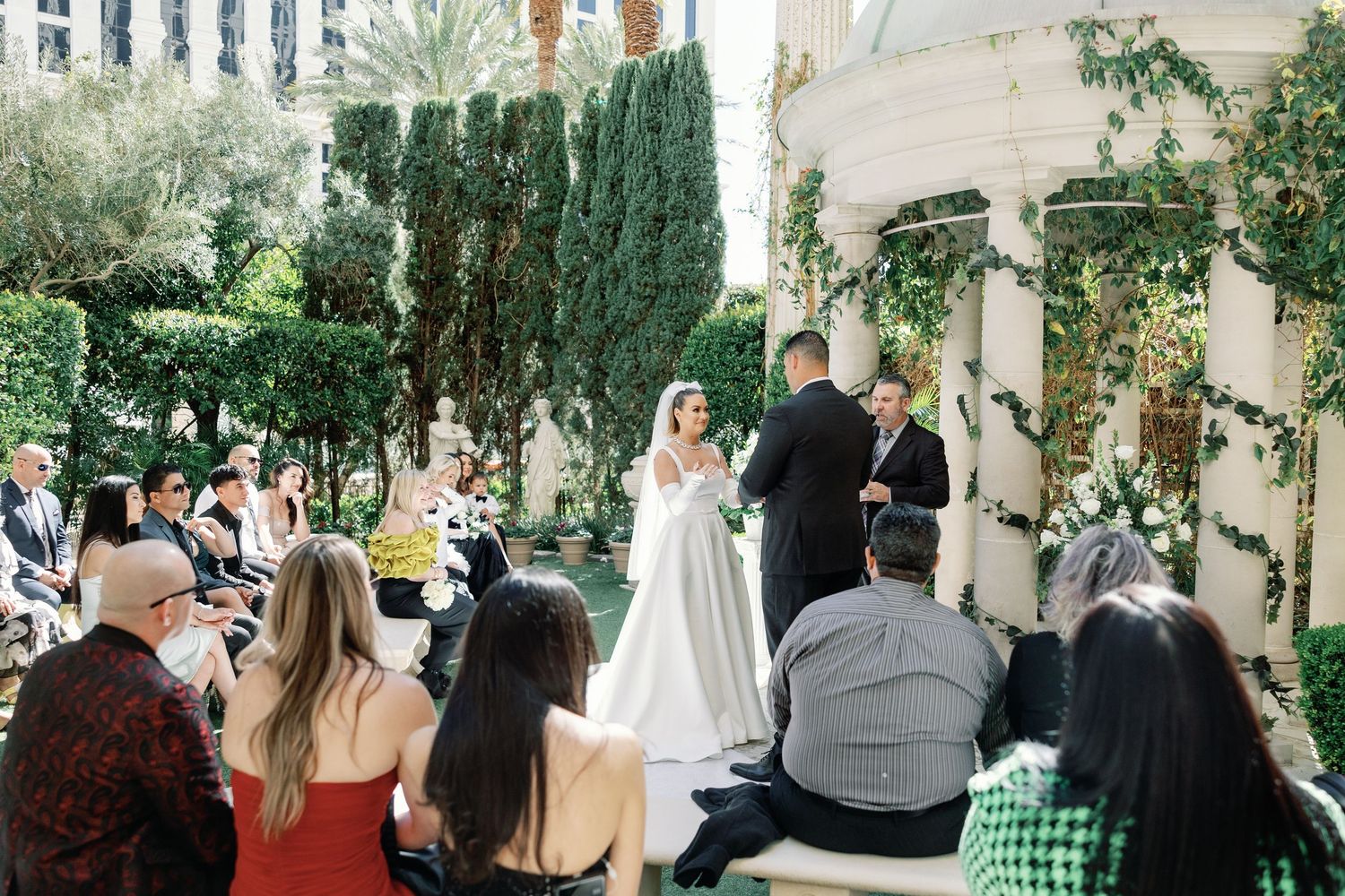 Outdoor wedding ceremony at a luxury Las Vegas venue with lush greenery, guests seated, bride and groom at the altar.