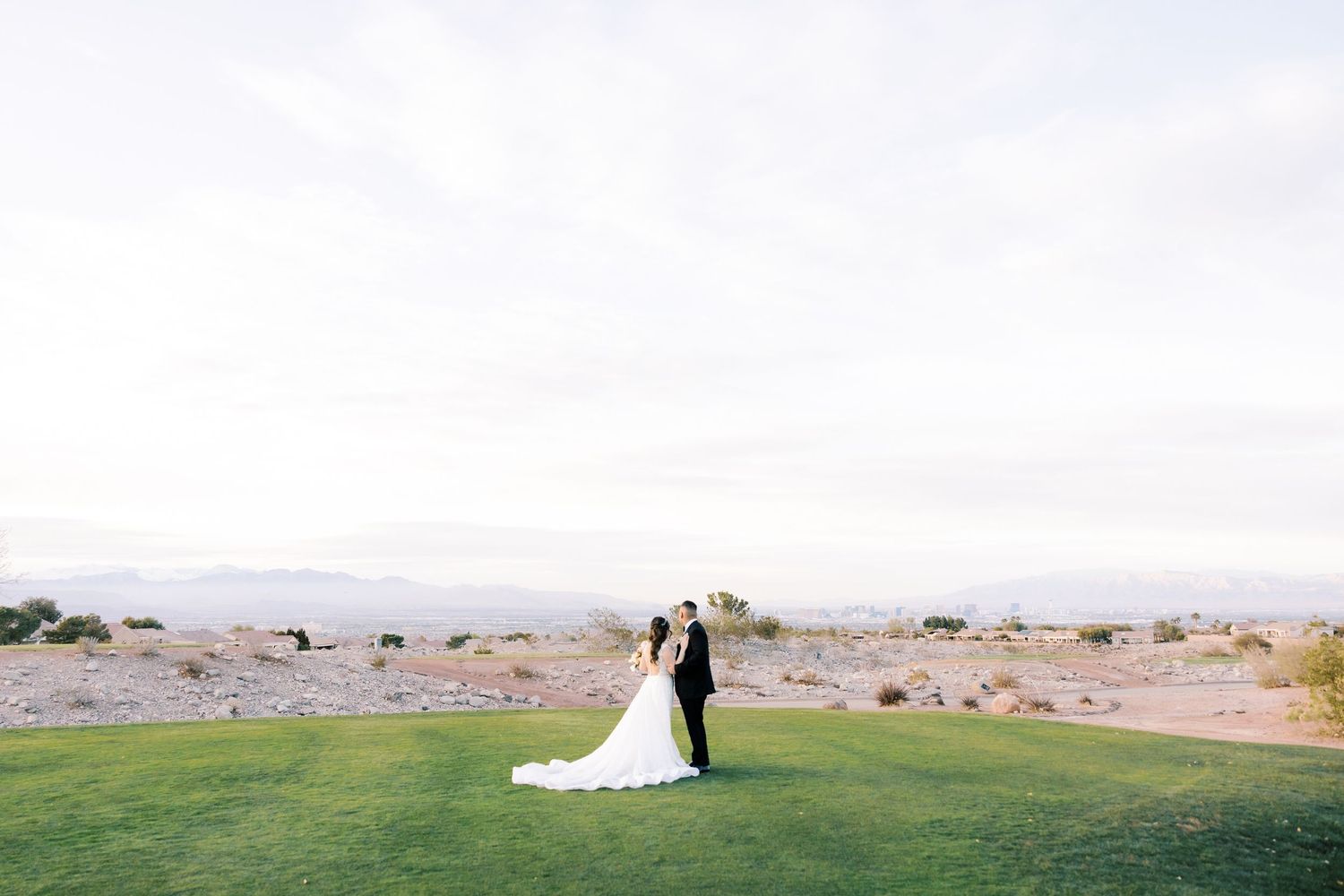 Bride and groom standing on lush green golf course with desert mountains backdrop on their wedding day.