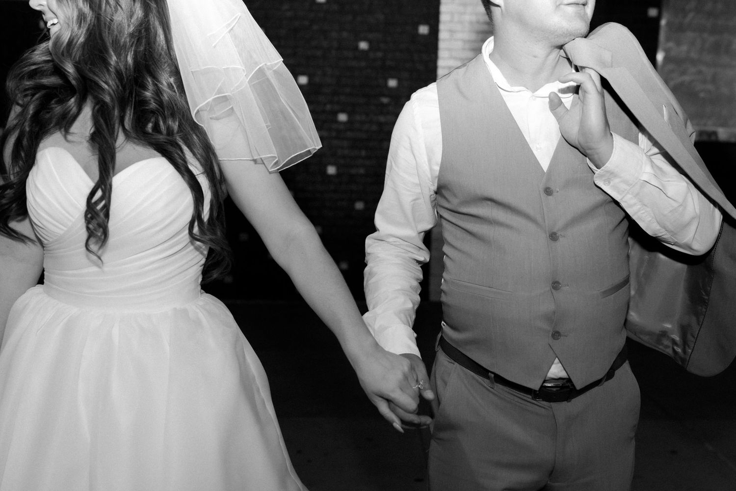 Black and white photo of bride and groom holding hands while dancing at their wedding reception.