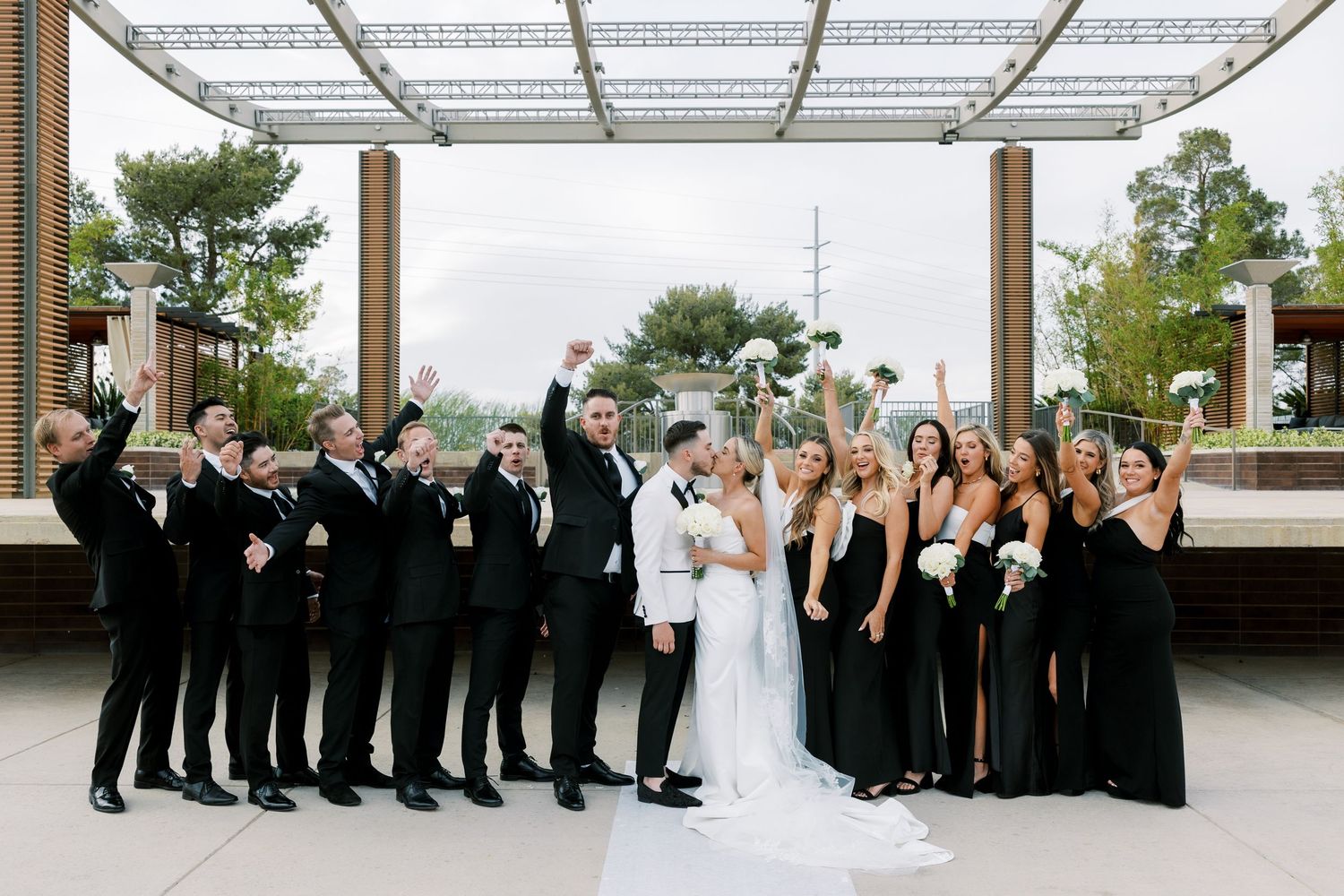 Wedding party in black and white attire celebrate outdoors, bride and groom centered with cheering bridal party.