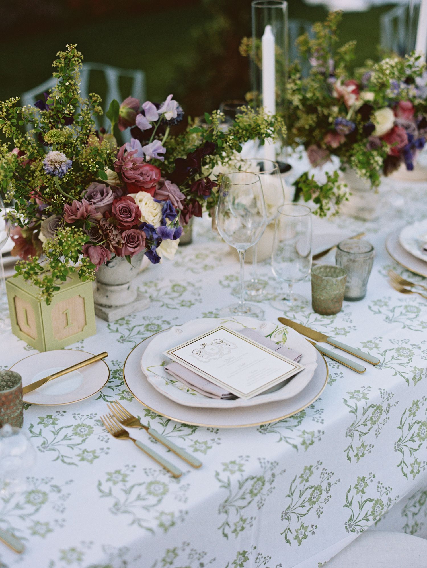 Elegant wedding table setting with floral centerpieces, gold cutlery, and a patterned green tablecloth.