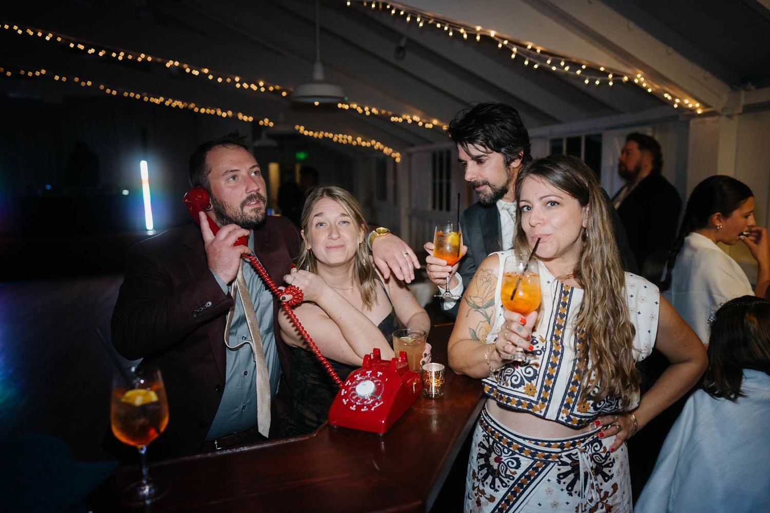 Group of friends enjoying cocktails at a nighttime party with string lights overhead.