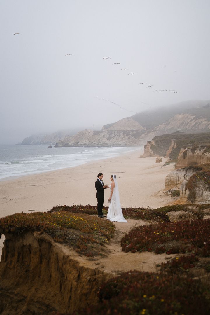 Cinematic coastal cliffside wedding scene captured in a misty, moody atmosphere at a Northern California beach.