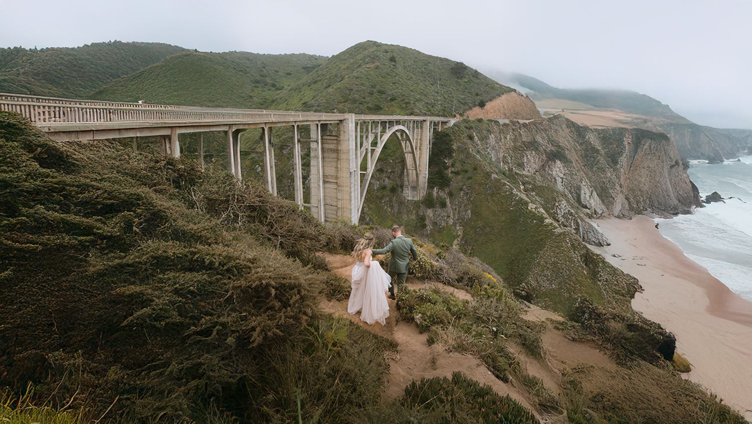 Scenic aerial view of the Bixby Creek Bridge along California's rugged Big Sur coastline with waves crashing below.