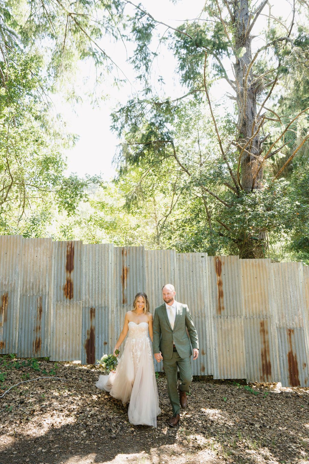 A couple enjoying a special outdoor moment in front of a rustic wooden fence surrounded by lush green trees.