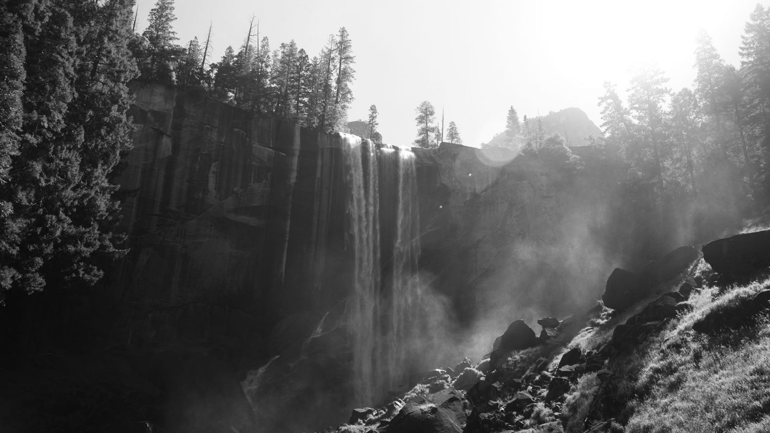 A scenic view of Yosemite's popular hike the mist trail  with tall evergreen trees silhouetted against a foggy sky.
