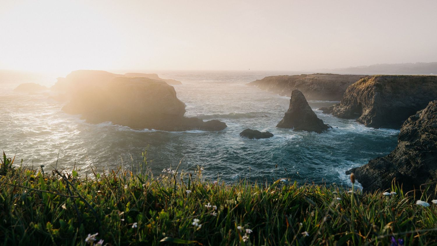 Dramatic coastal panorama of rugged cliffs and crashing waves along the Pacific coastline during a golden sunset.