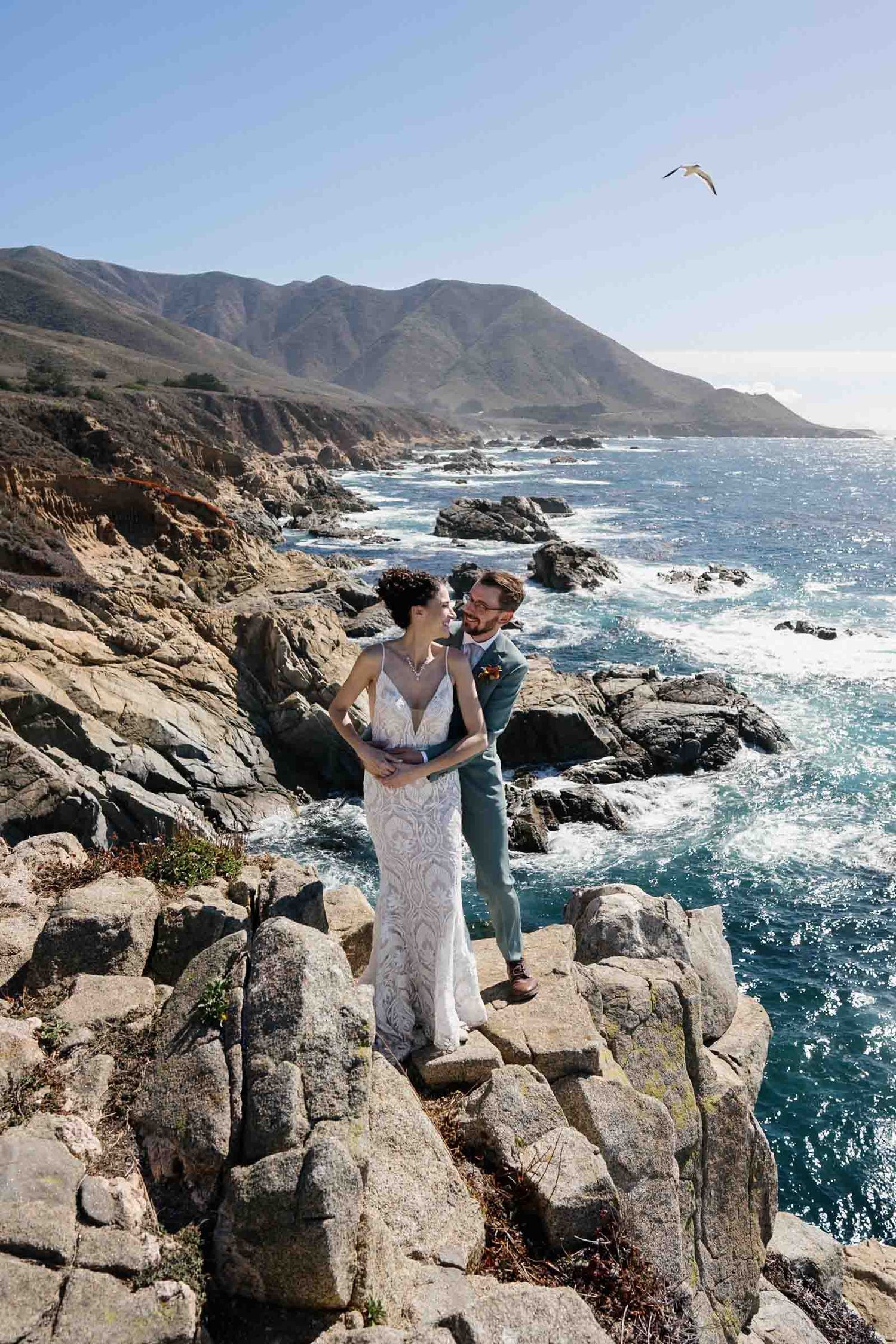 Dramatic coastal wedding photos on rocky cliffs overlooking the crashing waves of Big Sur, California.
