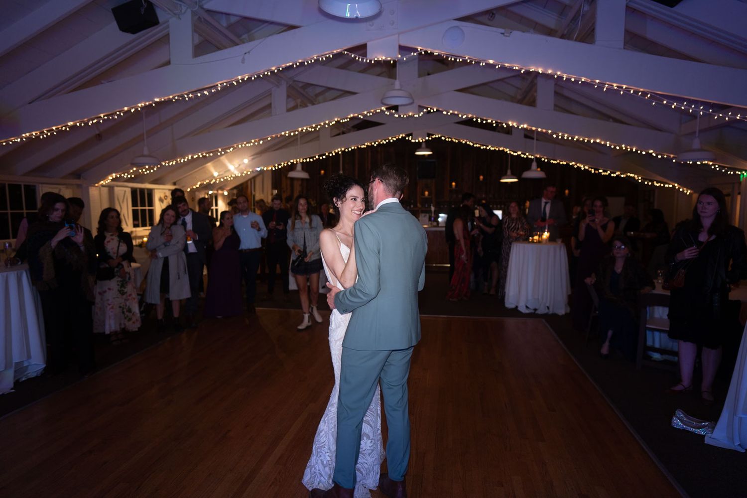 A couple shares their first dance at a wedding reception under twinkling string lights in an elegant tent venue.