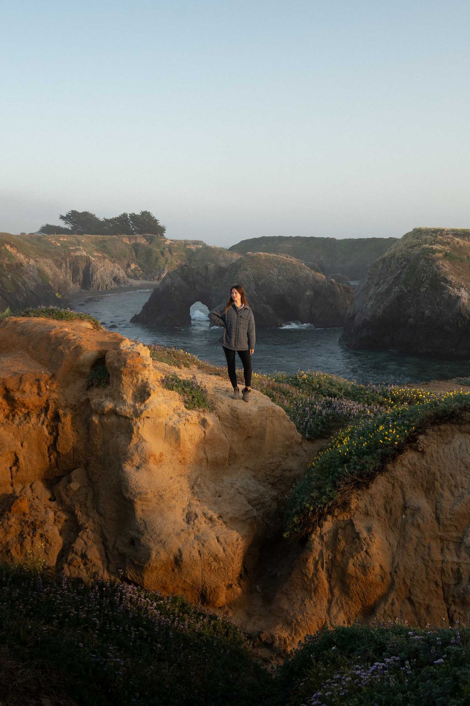 Scenic coastal view of rugged cliffs and natural rock arch formation at Mendocino Headlands during golden hour.