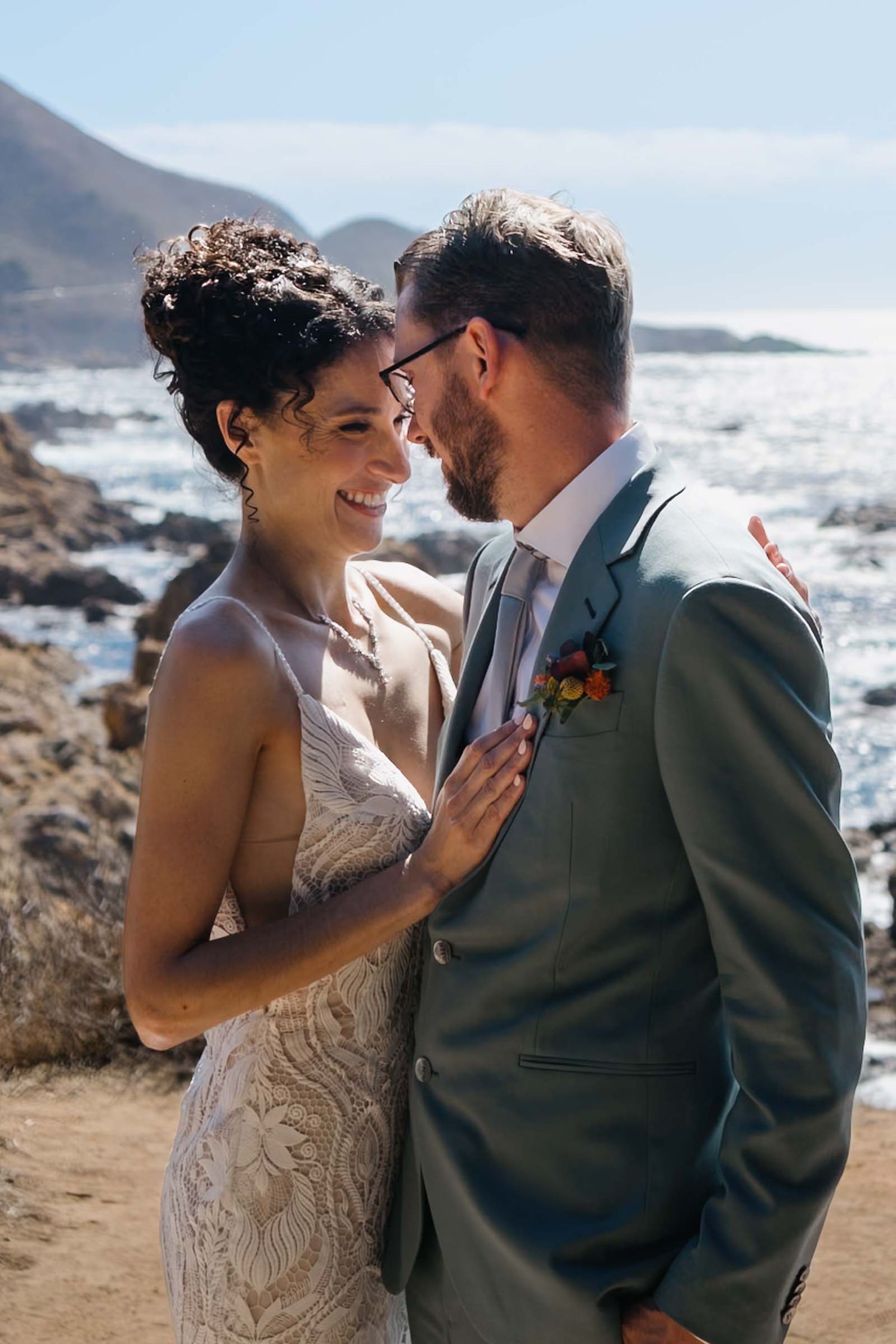 A romantic wedding couple shares an intimate moment on a coastal cliff overlooking big sur.