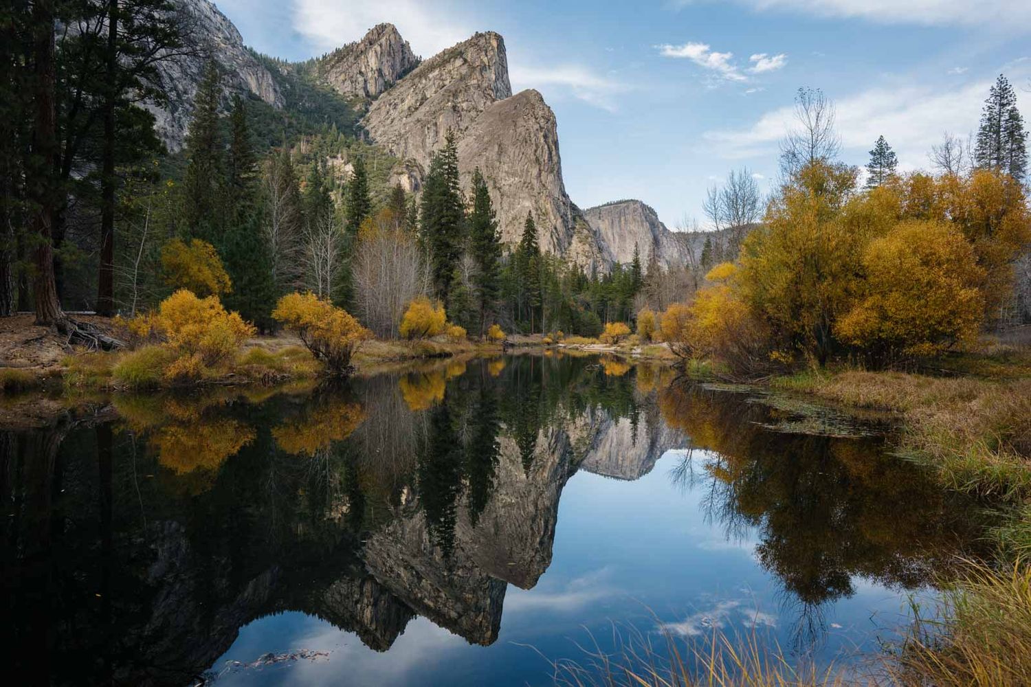 Stunning panoramic view of Yosemite Valley with granite cliffs reflected in calm lake waters during autumn season.