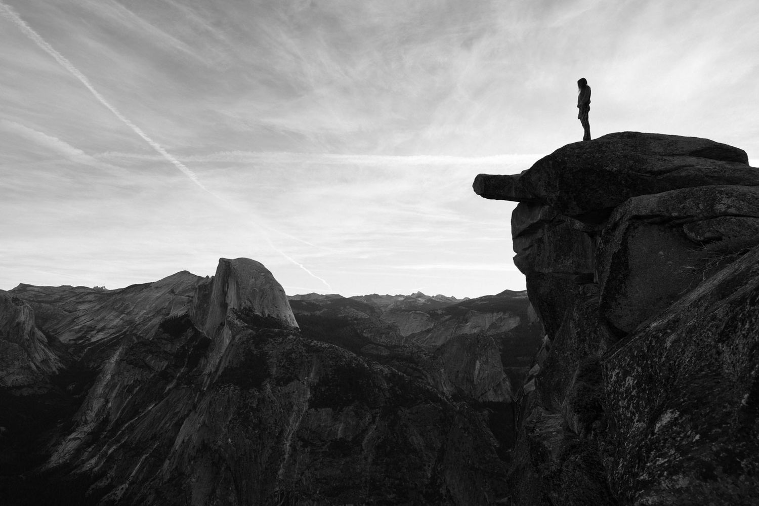 A silhouetted figure stands atop a mountain ridge overlooking Half dome from glacier point.