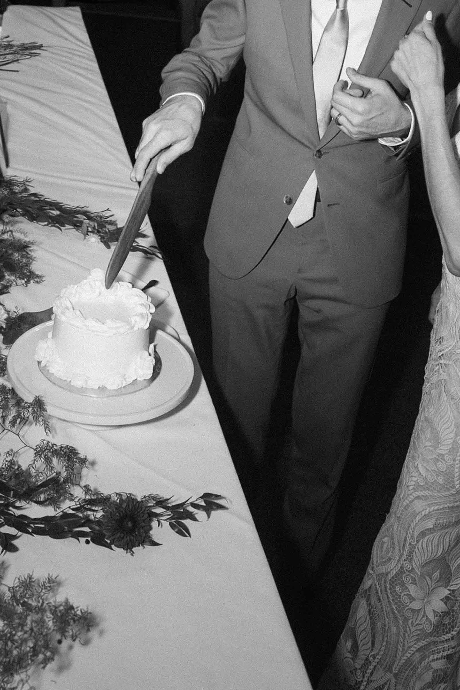 A vintage black and white wedding photo showing the traditional cake cutting moment at a reception.
