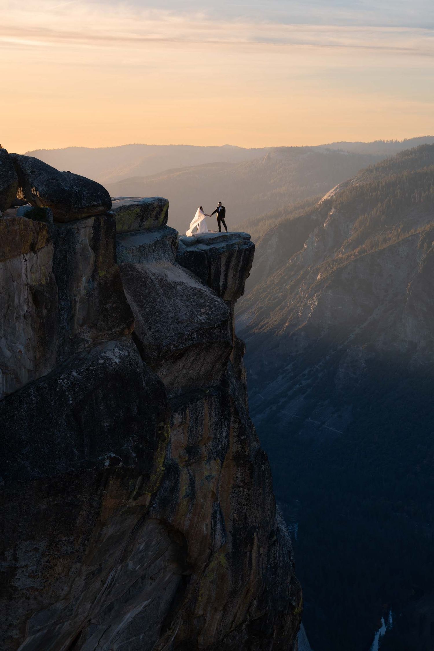 Silhouetted figures stand on Taft Point's dramatic cliff edge overlooking Yosemite Valley at sunset.