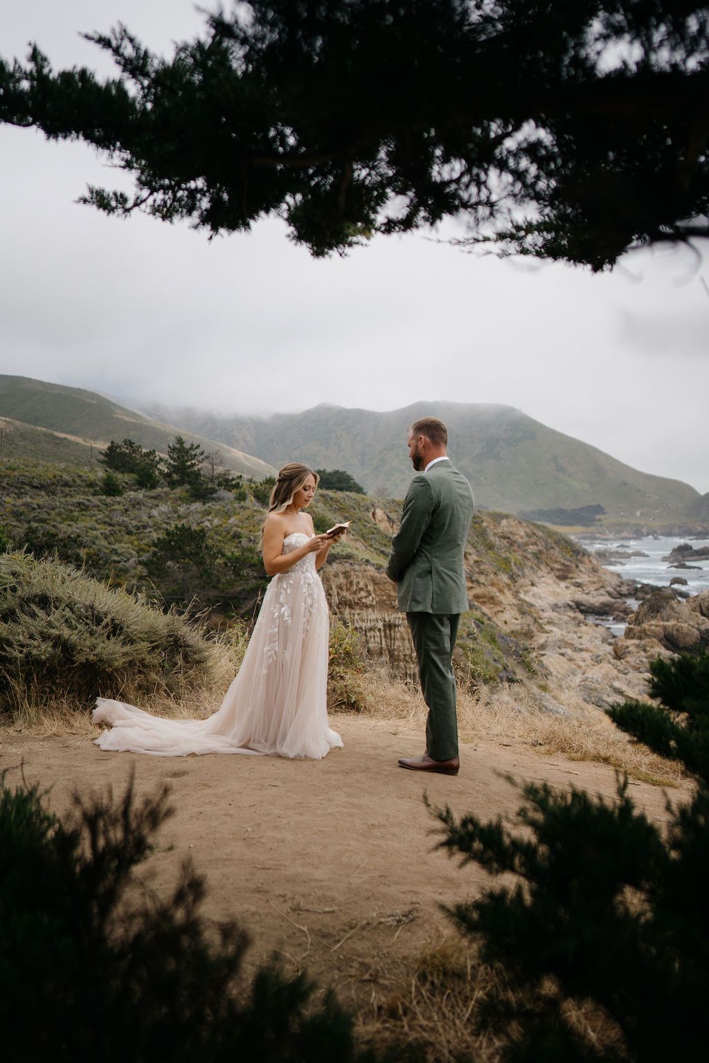 A couple shares their wedding vows on a scenic cliff overlooking the rugged California coastline at sunset.
