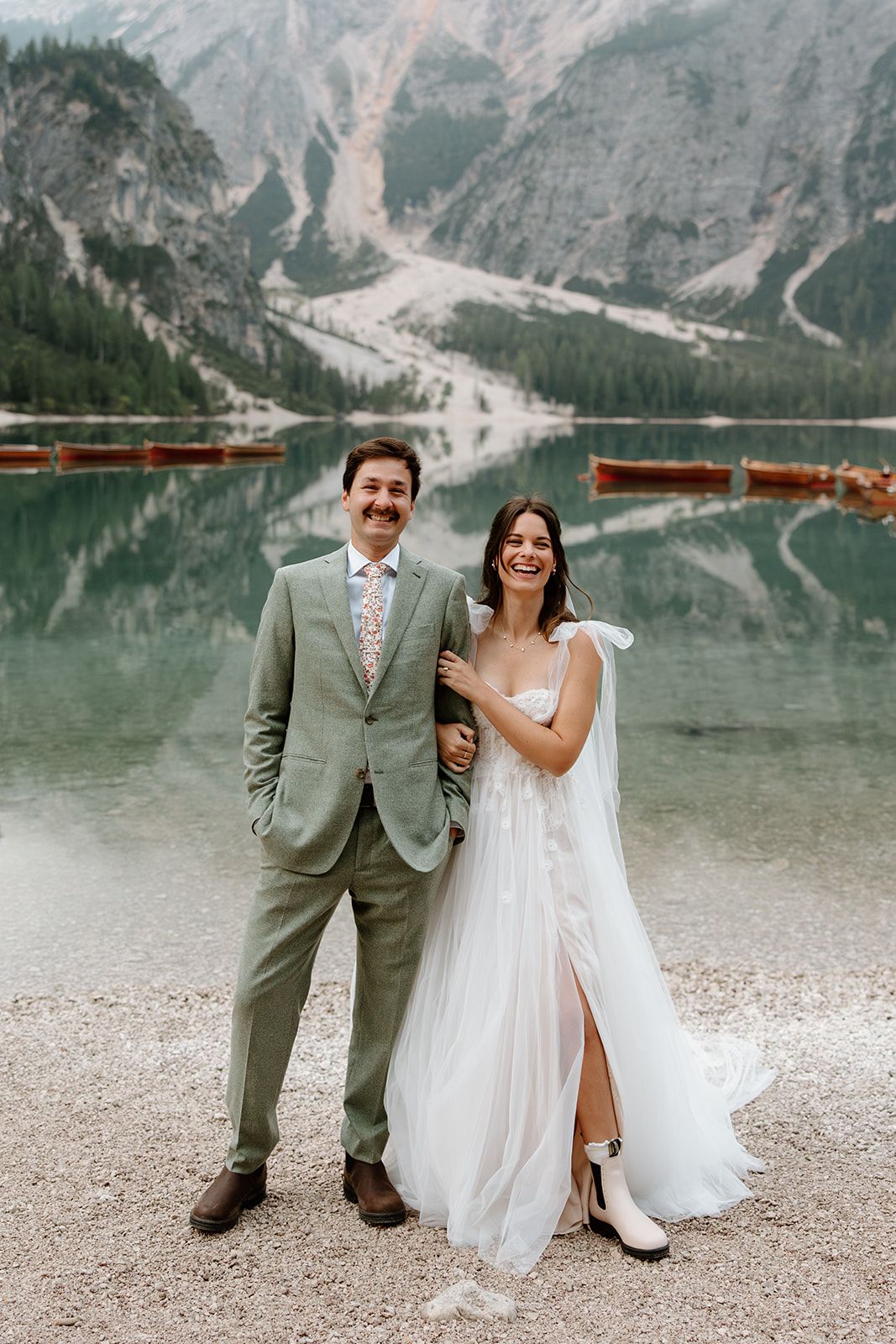 A wedding couple poses against the stunning backdrop of a mountain lake with dramatic peaks and turquoise waters.