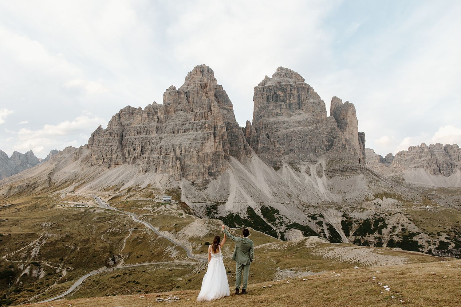 Panoramic view of rugged mountain peaks and rocky cliffs in the Dolomites under a cloudy blue sky.