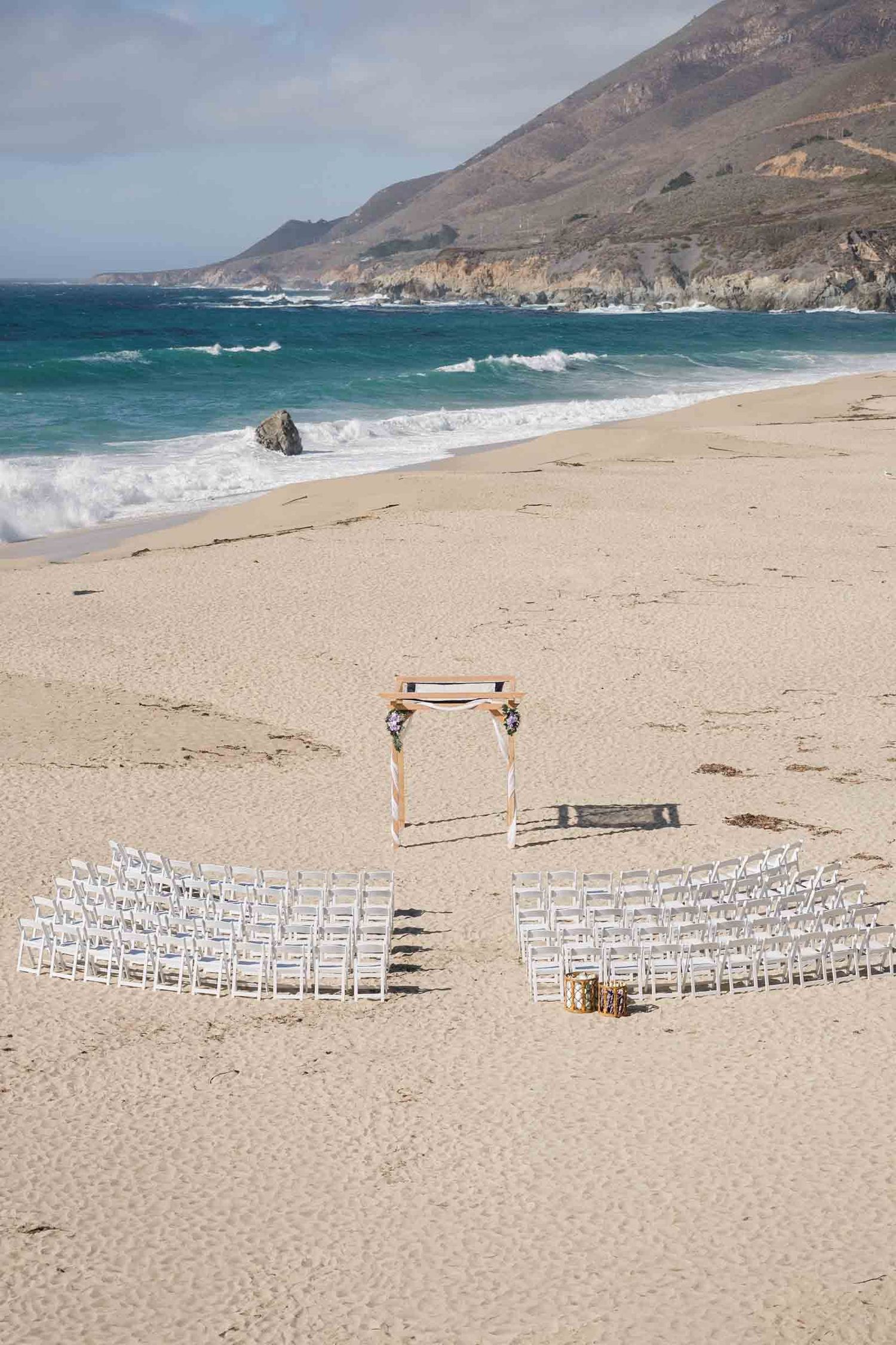 Garrapata beach wedding ceremony being set up with wooden chairs and a chuppa.