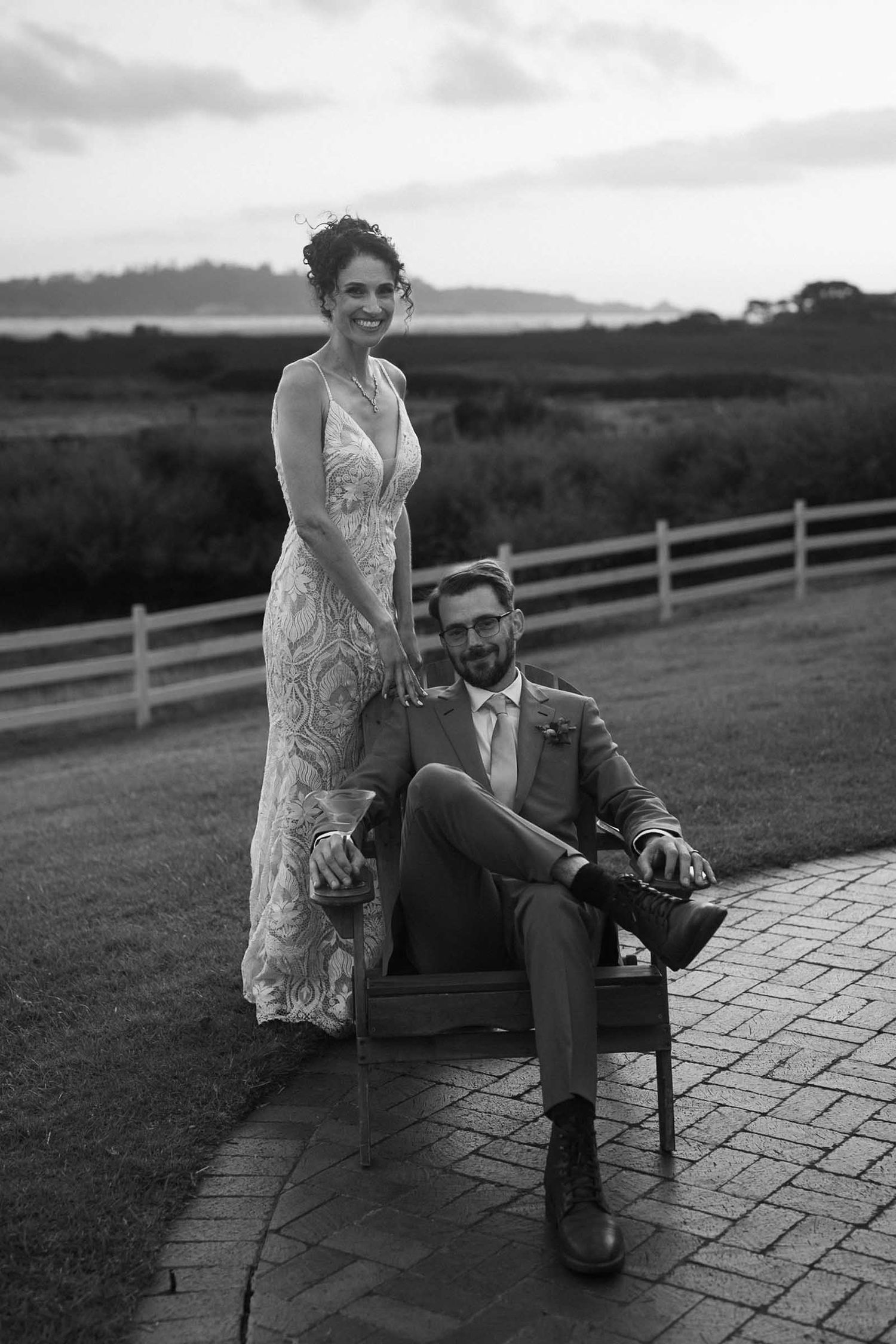 A black and white romantic portrait of a couple posing together on a stone patio with rolling hills in the background.