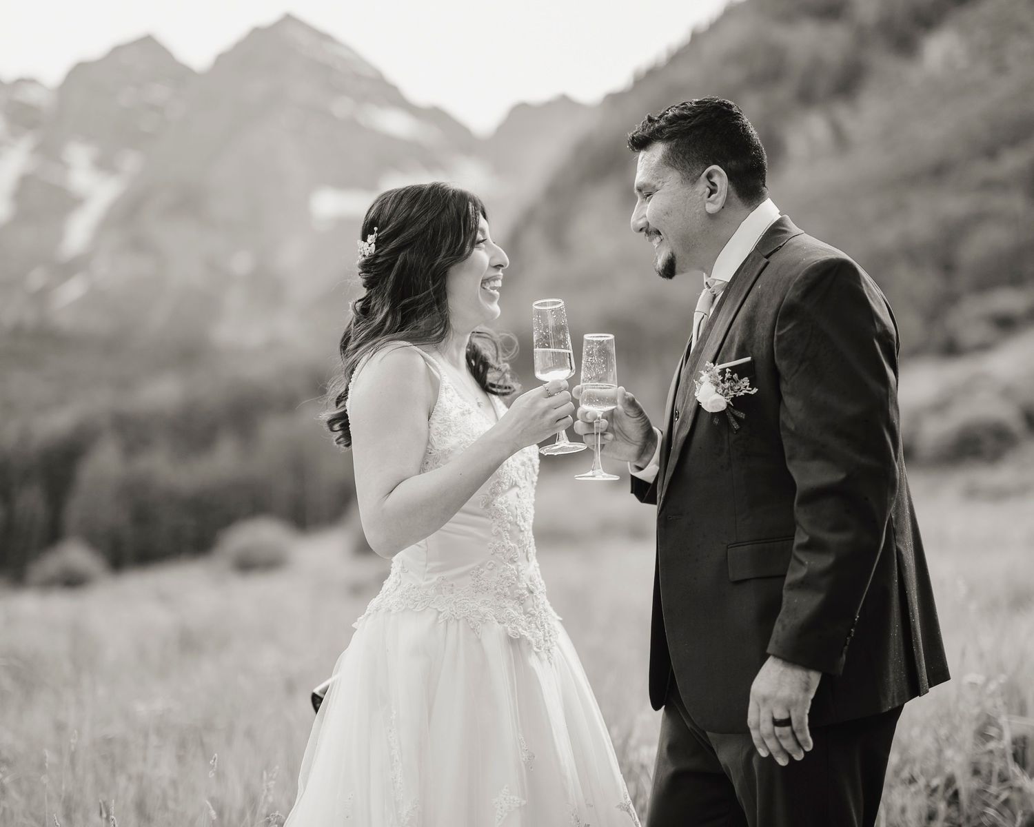 A black and white photo of newlyweds toasting with champagne glasses against a scenic mountain backdrop.