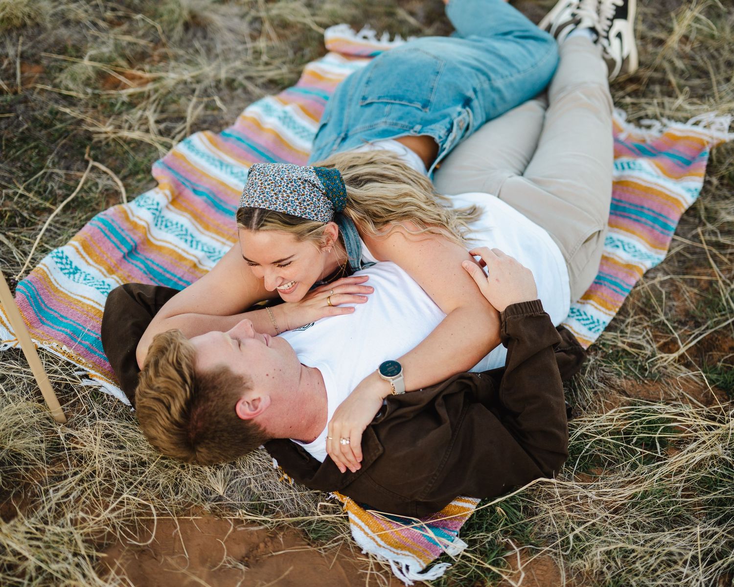 A romantic couple lying together on a striped blanket outdoors sharing an intimate moment.