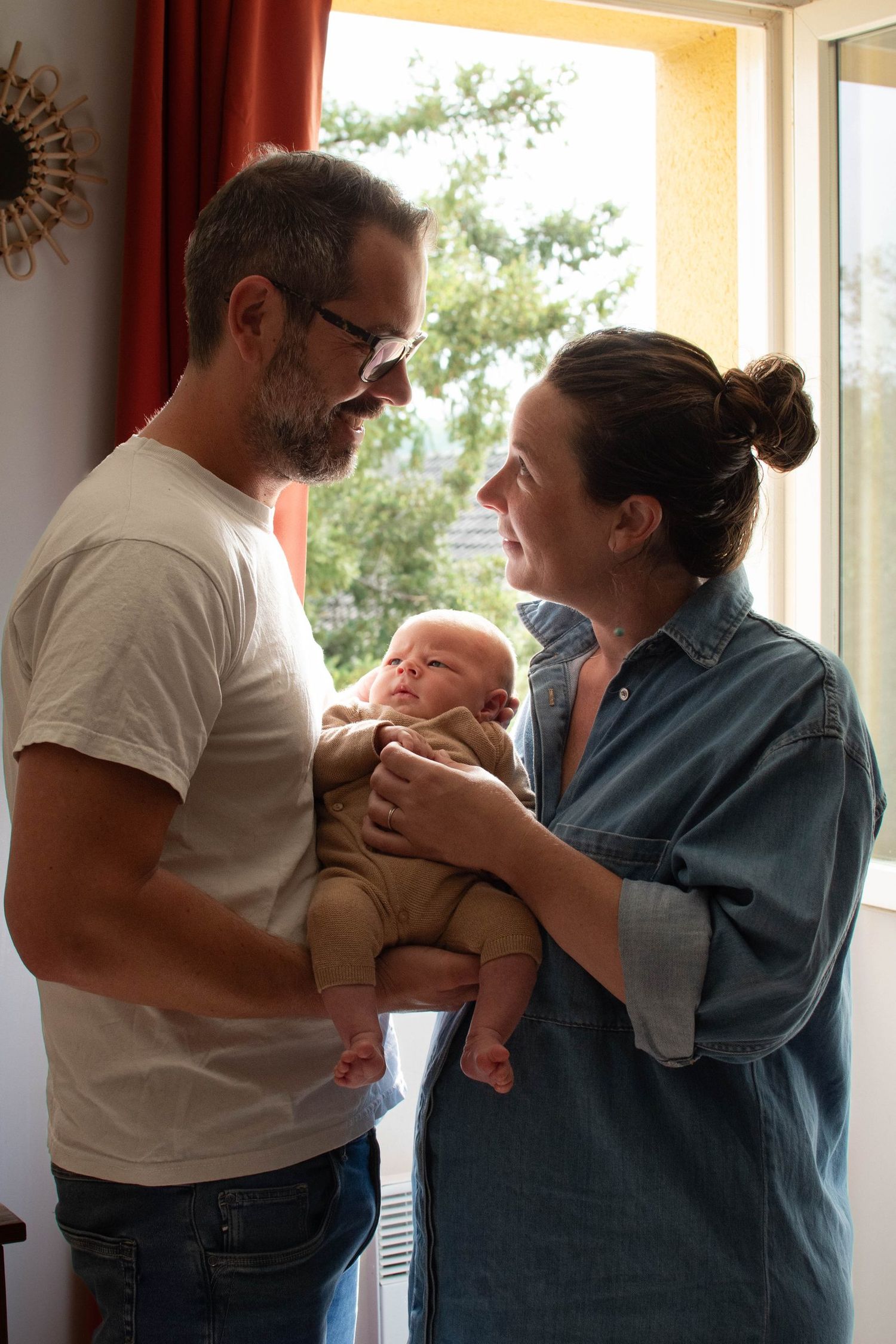 Jeunes parents regardant leur bébé près de la fenêtre