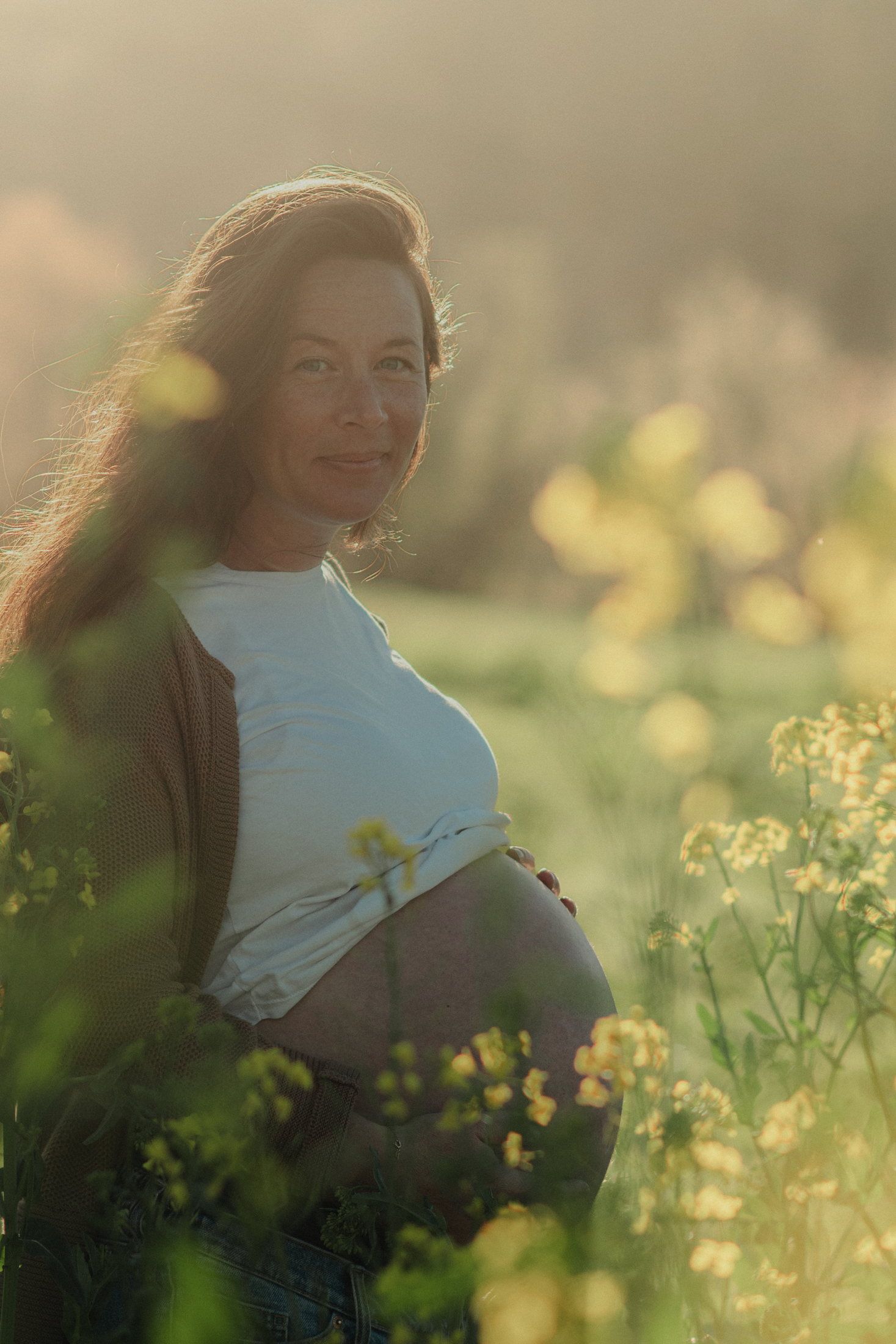 Future maman dans un champ de colza baigné de lumière