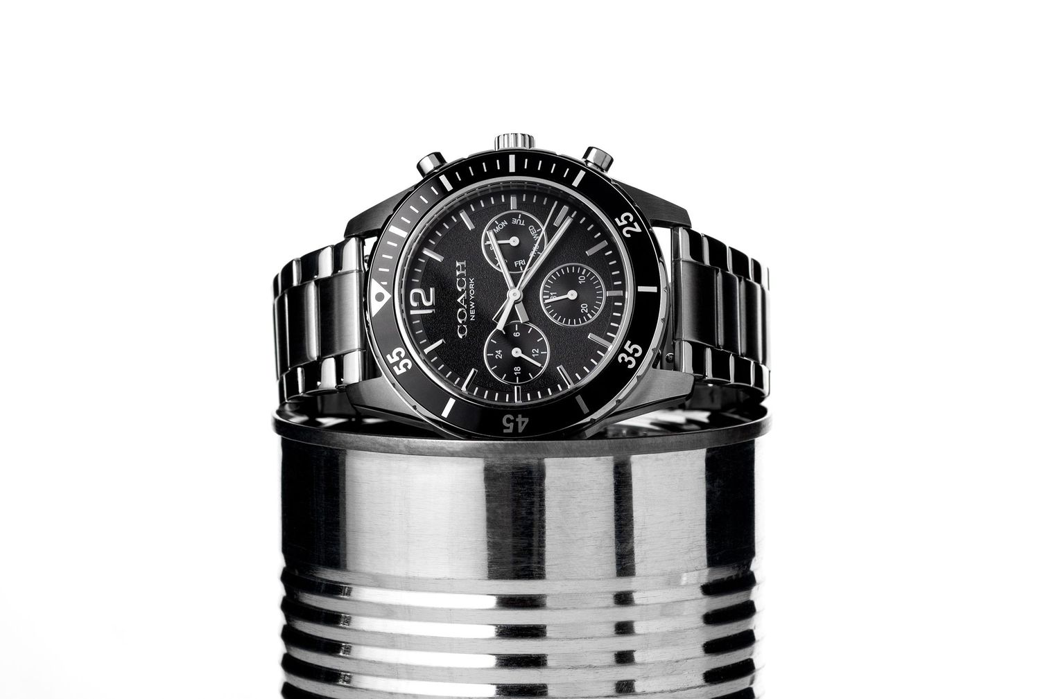 Black and white chronograph wristwatch with metal bracelet displayed on a tin can.
