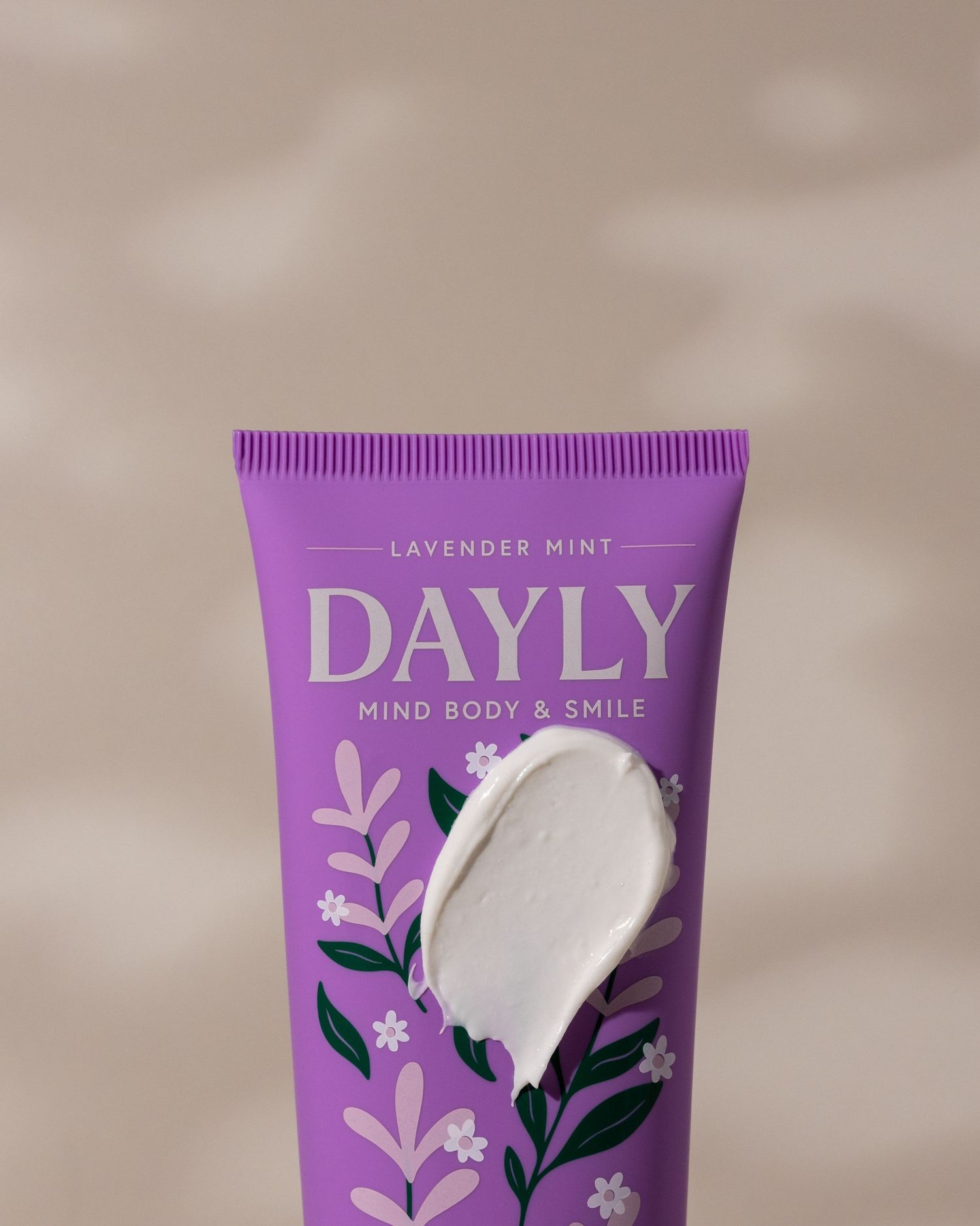 Purple tube of Dayly Lavender Mint Mind Body & Smile cream with a white swipe of product on floral packaging.