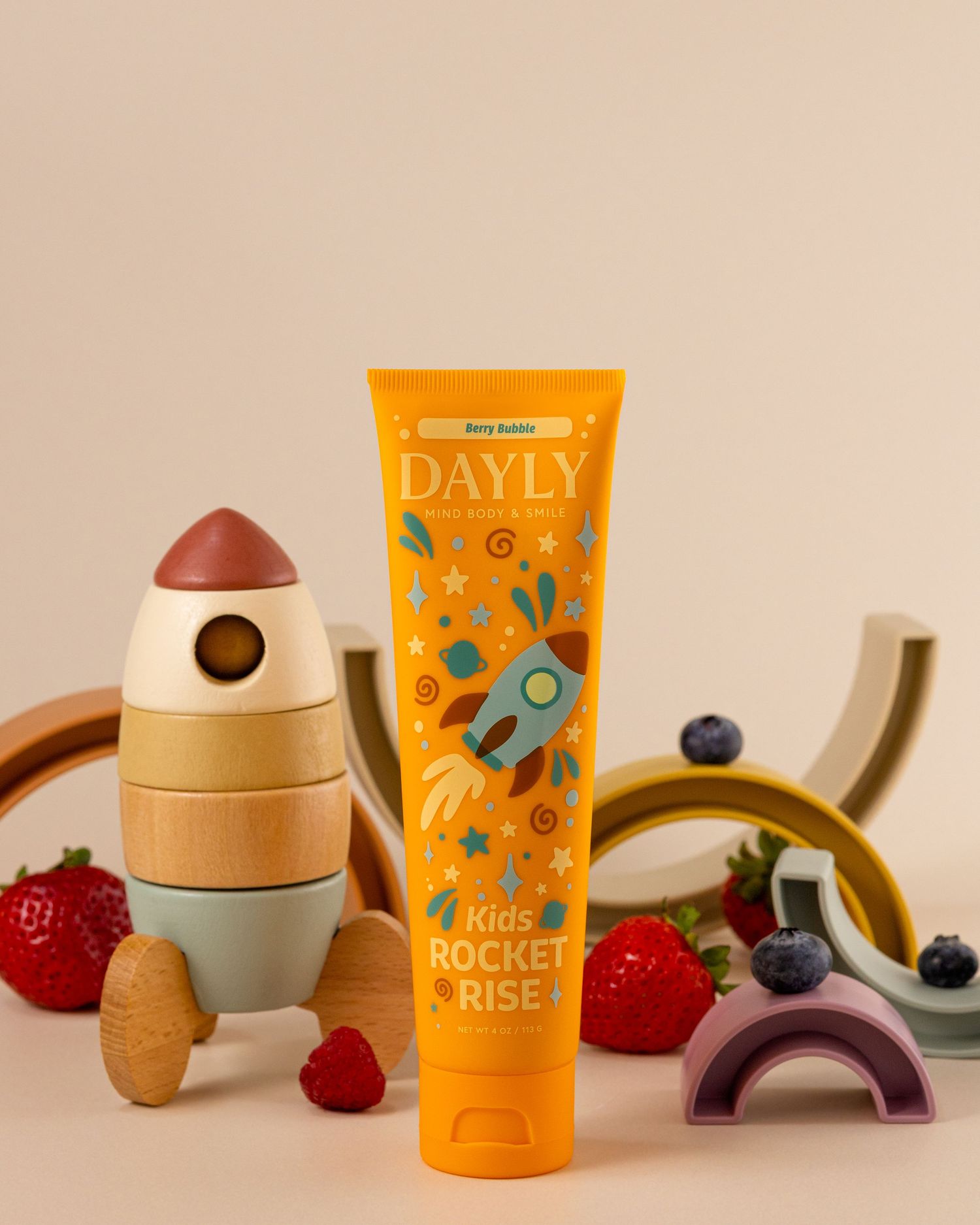 Dayly Kids Rocket Rise berry apple toothpaste tube in orange packaging with toy rocket and fresh berries.