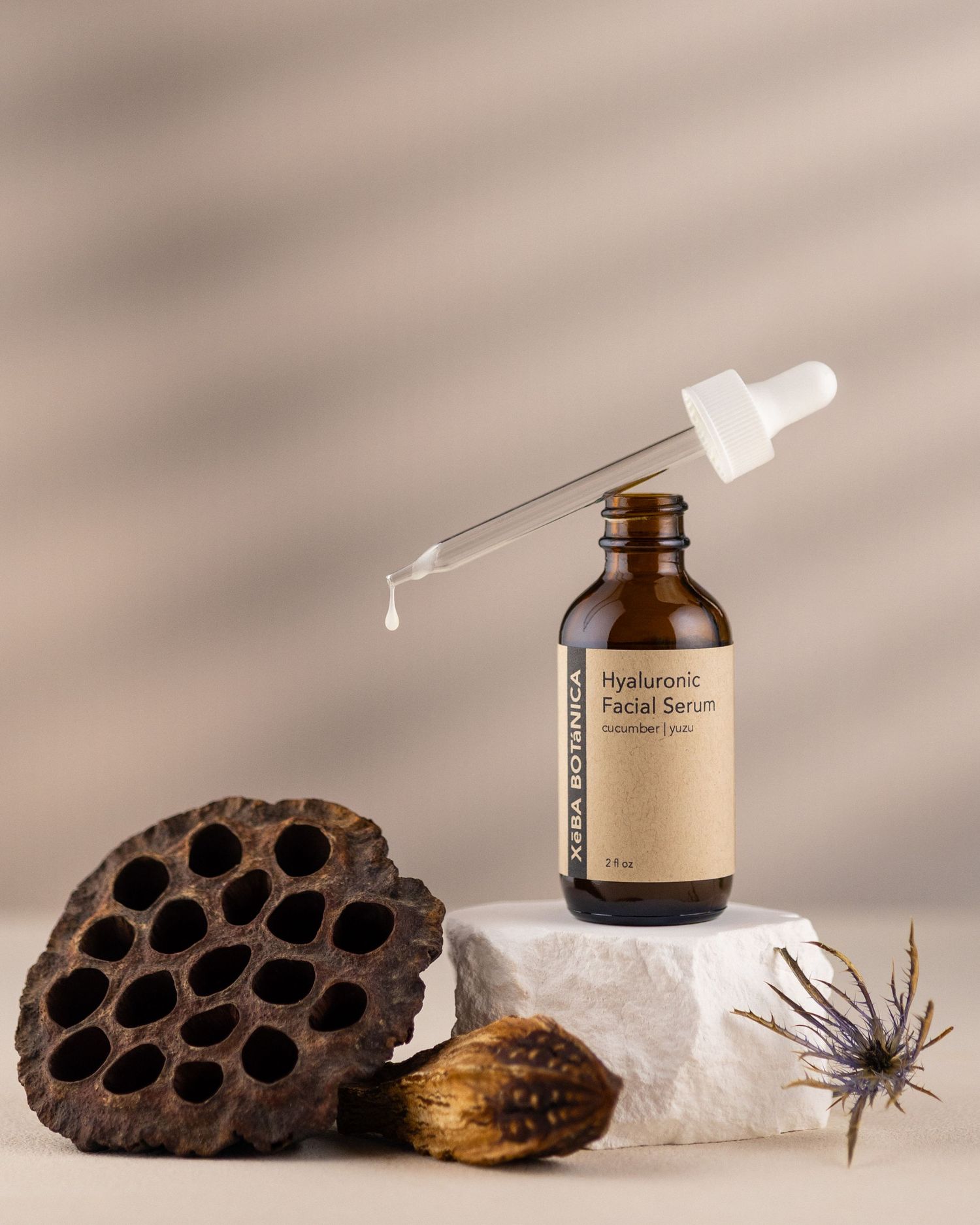 Xeba Botanica Hyaluronic Facial Serum dropper bottle with a drop falling, beside a lotus pod.