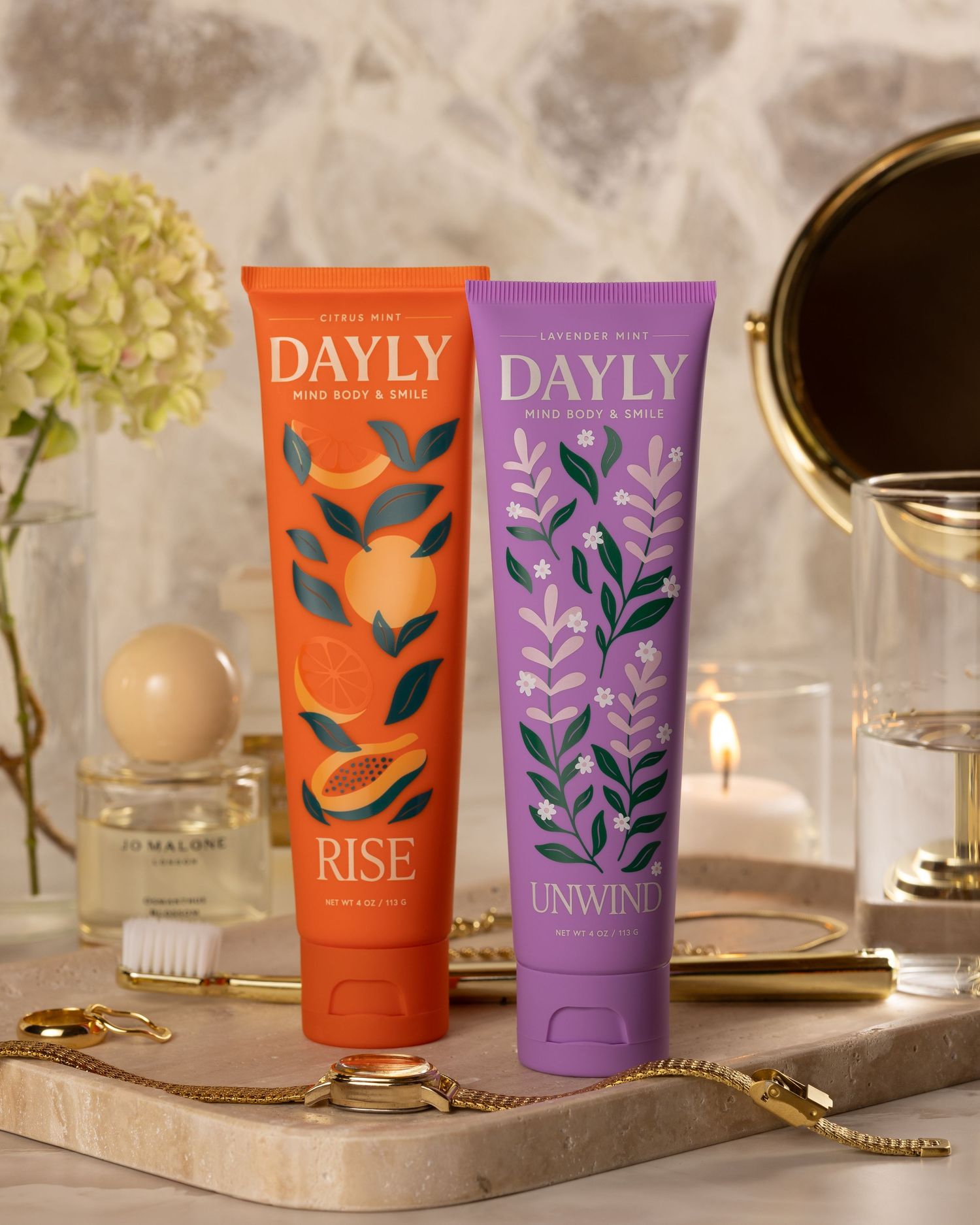 Two DAYLY mind body and smile tubes, Rise in orange and Unwind in purple, displayed on a vanity tray.