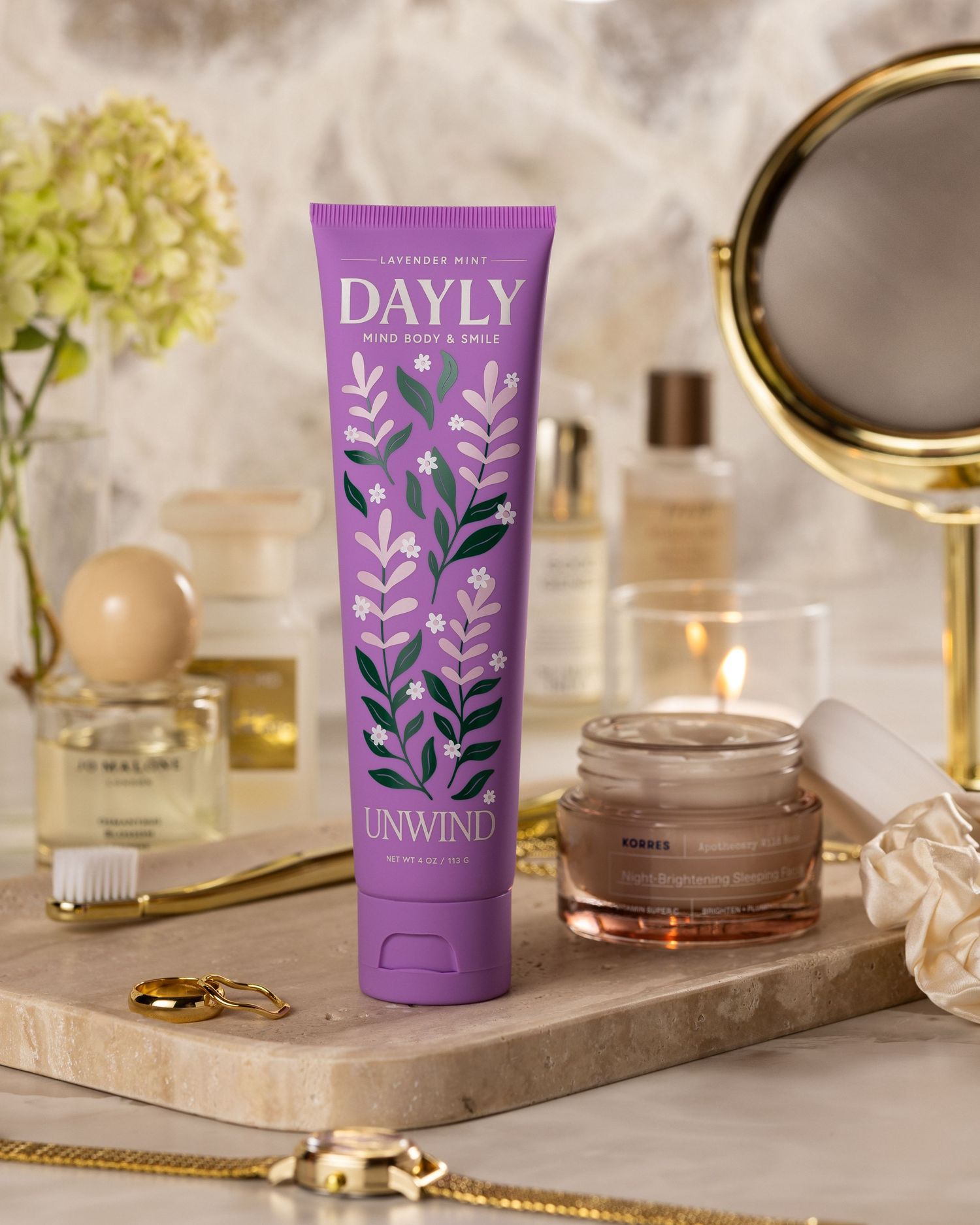 Dayly Unwind lavender mint body and mind cream tube in purple floral packaging on a marble tray with beauty products.
