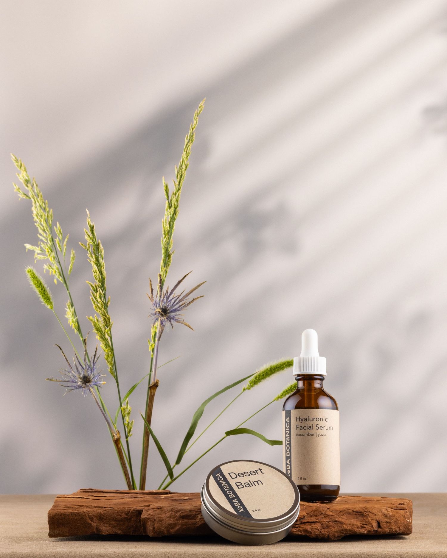 Xeba Botanica Hyaluronic Facial Serum and Desert Balm displayed with wildflowers on rustic wood.