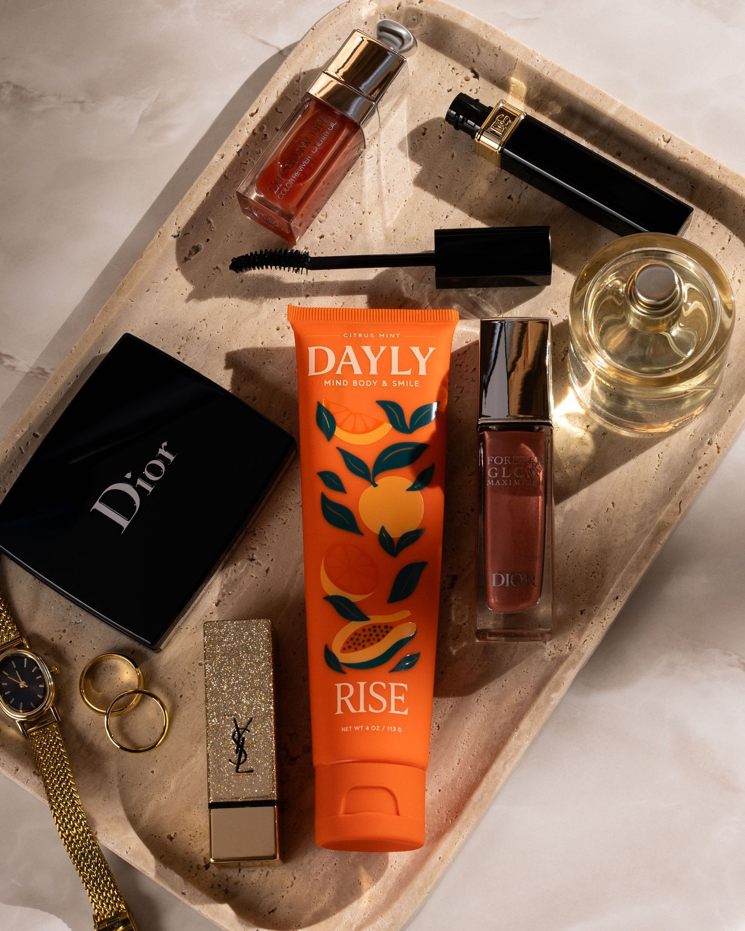 Luxury beauty flatlay featuring Dior, YSL, and Dayly Rise skincare products arranged on a marble tray.
