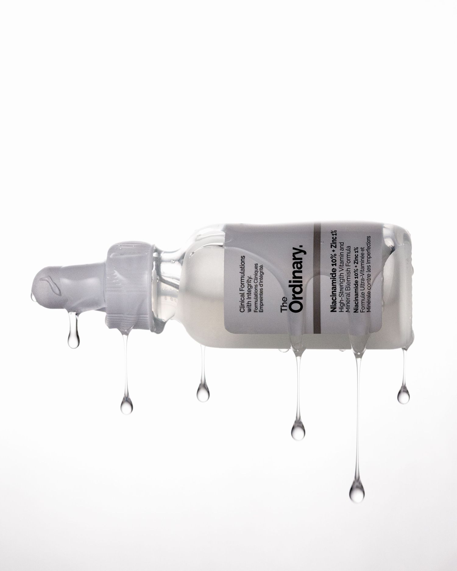 The Ordinary Niacinamide 10% + Zinc 1% serum bottle with multiple liquid drops falling on white background.