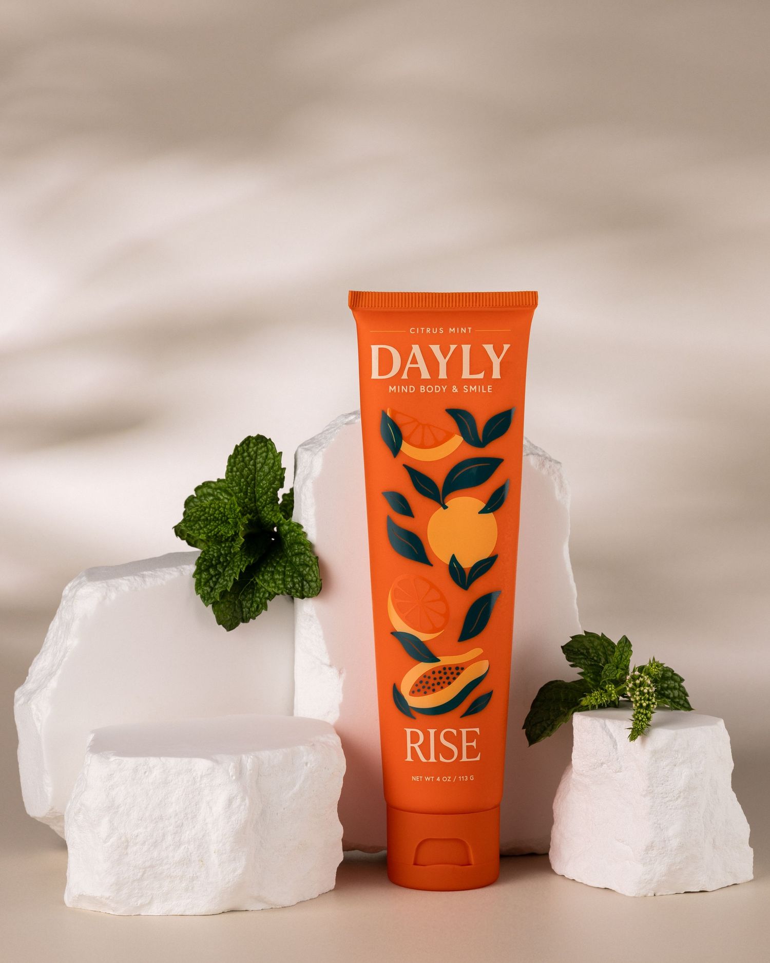 Orange tube of Dayly Rise citrus mint hand body and face cream displayed on white stone blocks with fresh mint leaves.