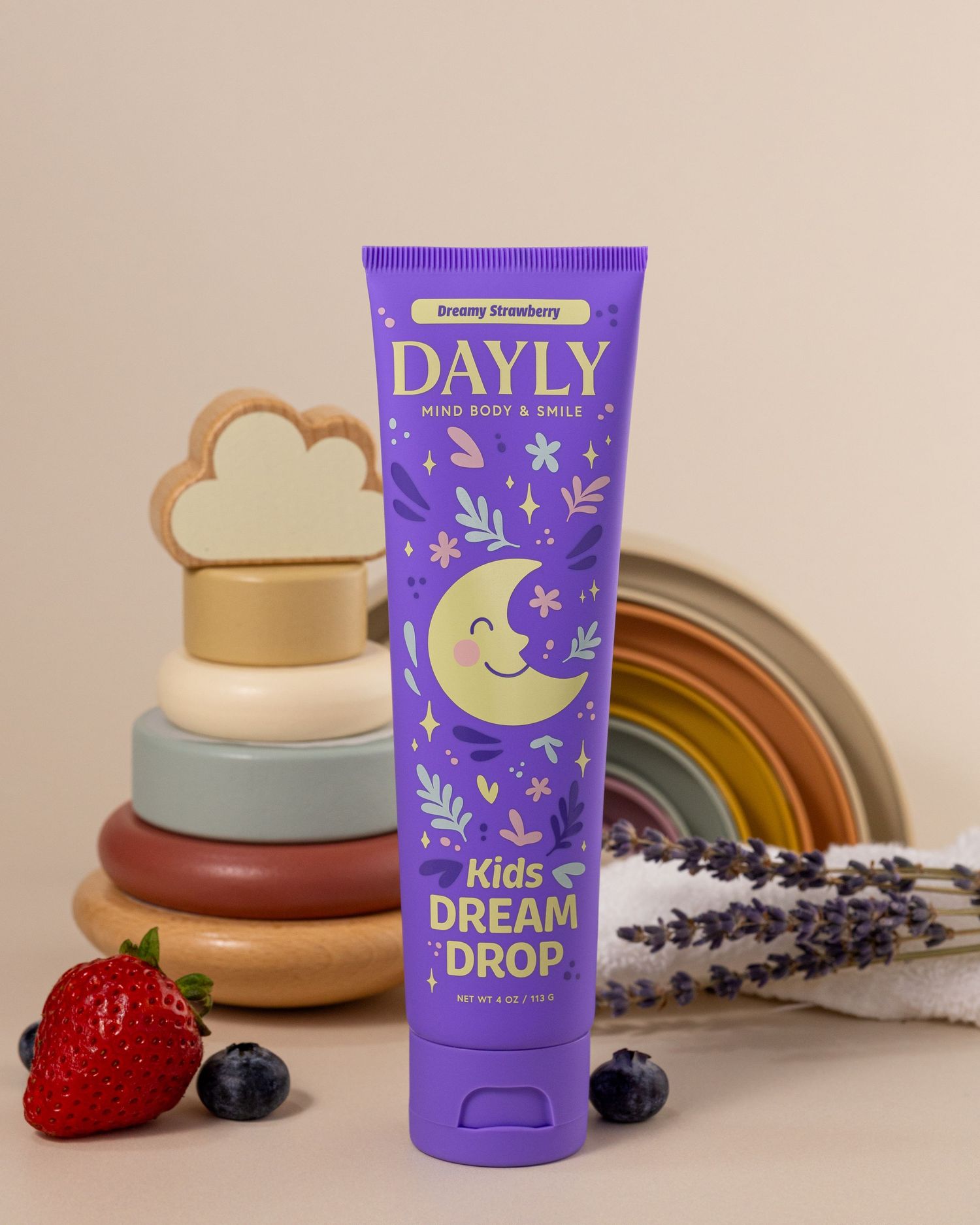 Dayly Kids Dream Drop purple tube in Dreamy Strawberry flavor, surrounded by lavender, berries, and colorful stacking toys.