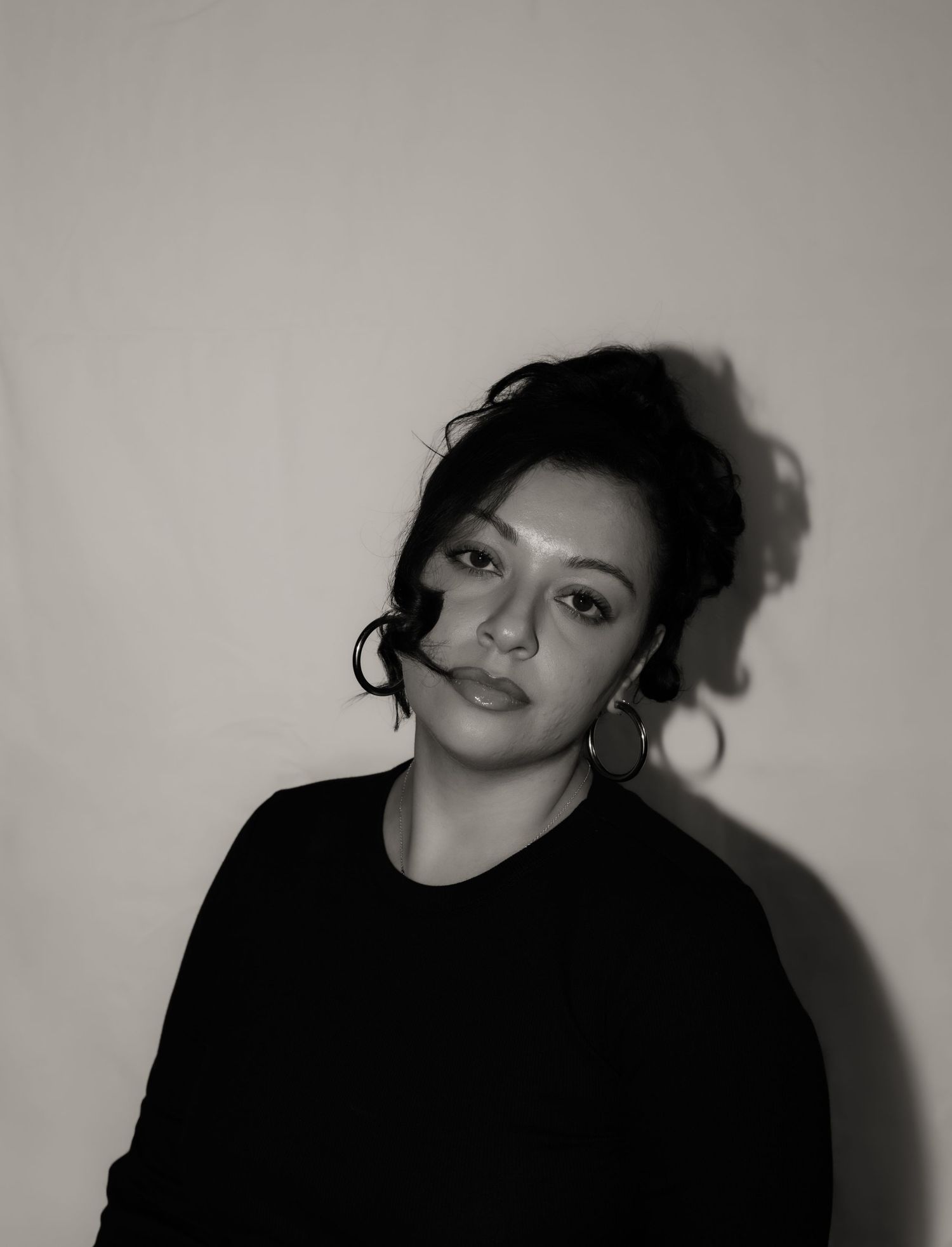 Black and white close-up portrait of woman with updo hairstyle and hoop earrings against light wall.