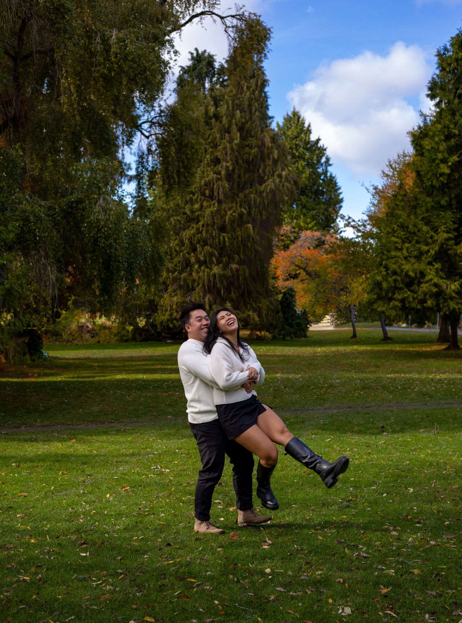 Joyful couple embracing and laughing in a lush green park with colorful autumn trees.