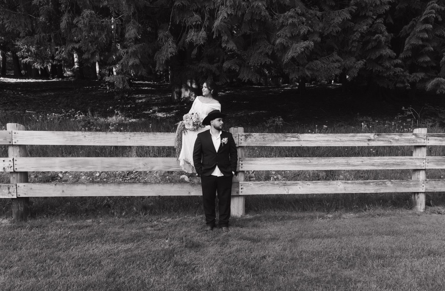 Black and white photo of a child in formal attire standing before a wooden fence in a park.