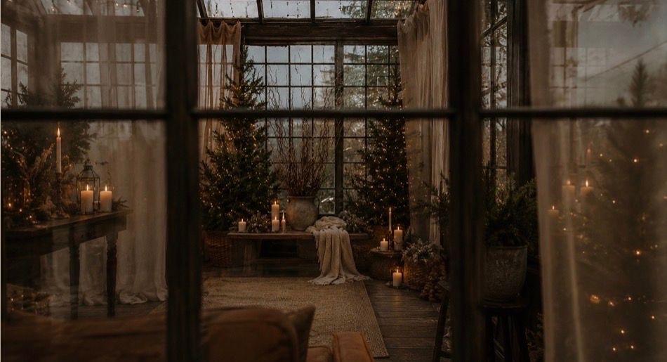 Cozy greenhouse wedding venue with Christmas trees, candles, and fairy lights creating a magical winter atmosphere.