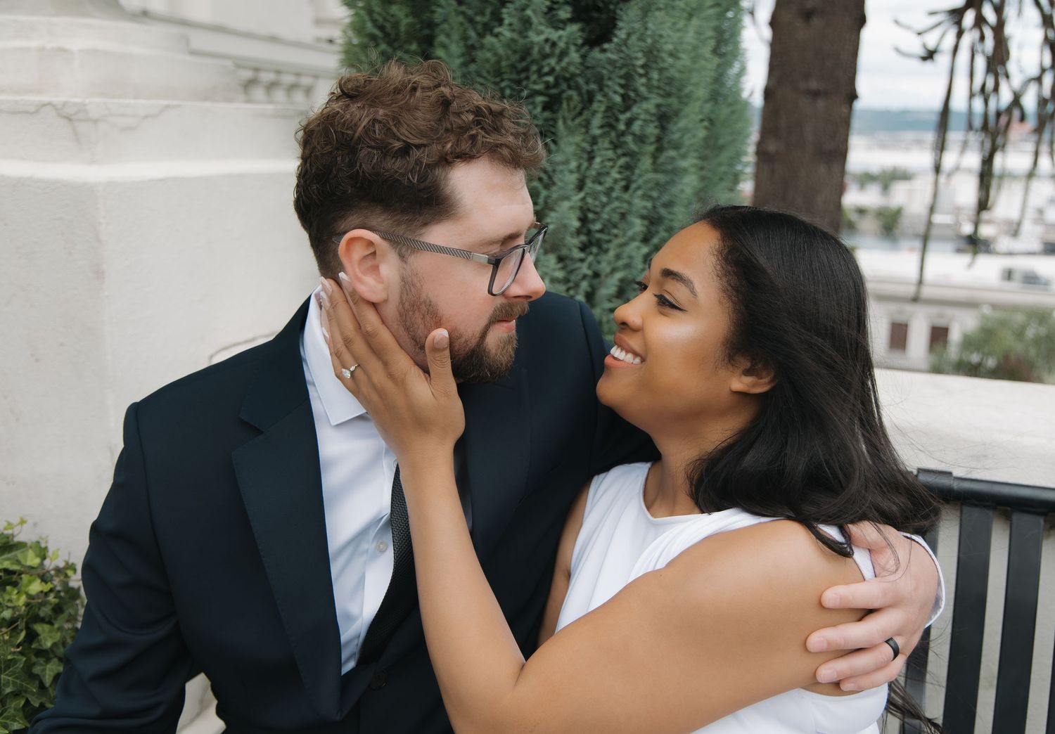 Smiling bride tenderly cups groom's face during romantic outdoor wedding portrait.