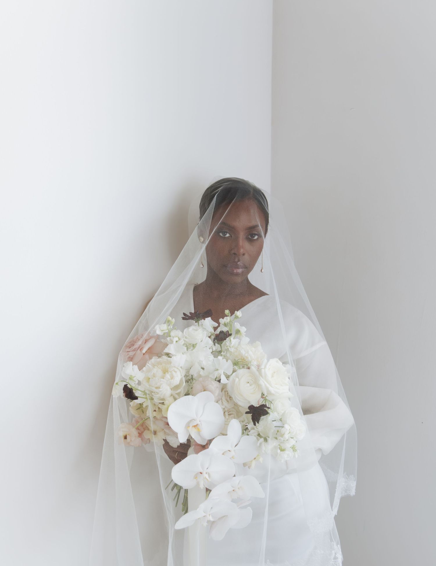 Elegant Black bride in white gown and veil holding white orchid bouquet in minimalist bridal portrait.