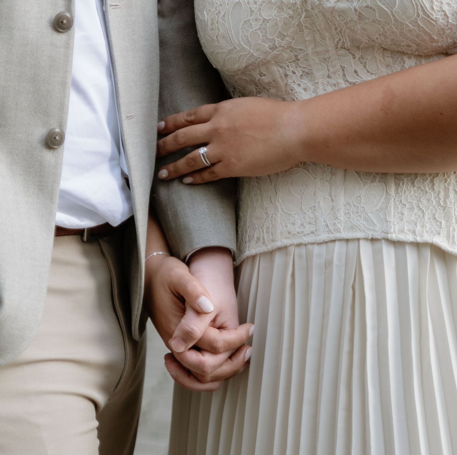 Close-up of couple holding hands at wedding, bride wearing diamond engagement ring in elegant attire.